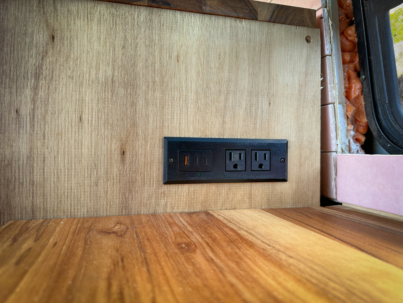 RV rental: Modern wooden wall with a built-in power strip featuring USB-A, USB-C, and two AC outlets for charging devices.