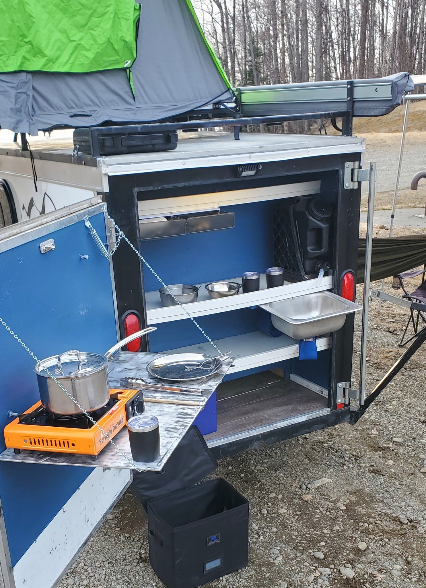 This RV rental features a convenient outdoor kitchen with a portable stove, sink, and storage for camping essentials.