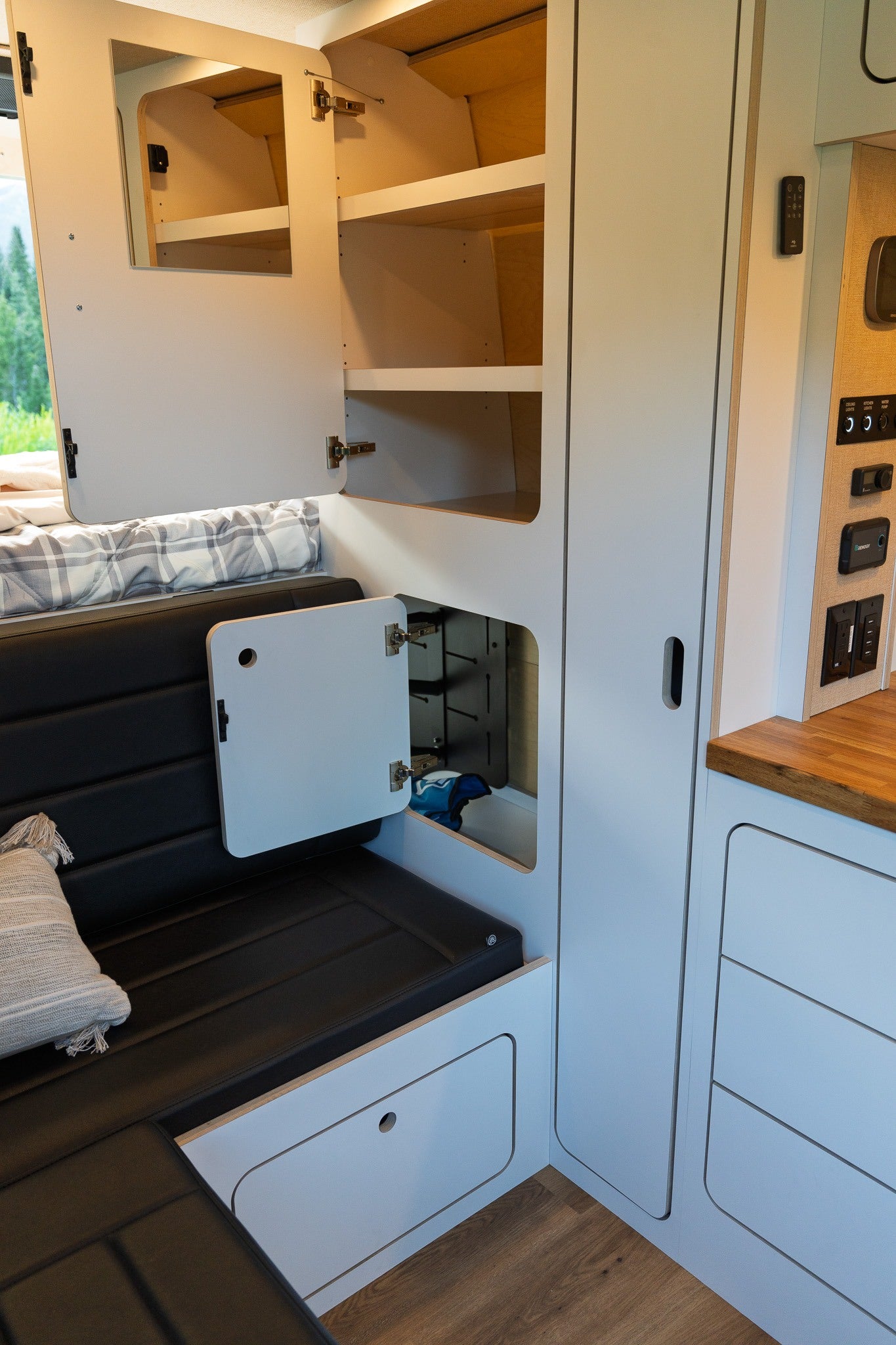 Inside this modern RV rental, light cabinets with shelves and a dark upholstered seating area provide ample storage and comfort for travel.