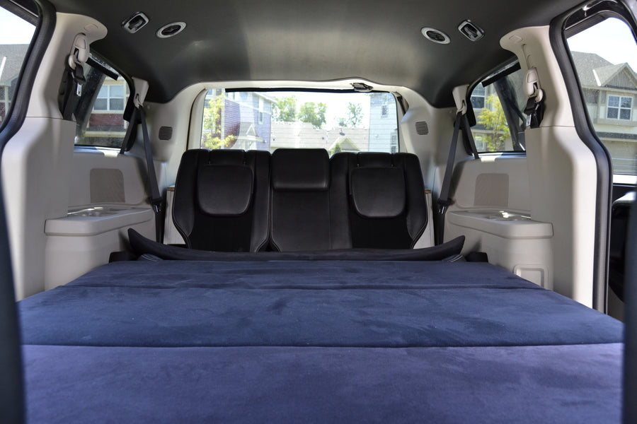 Cozy vehicle interior, perfect for an RV rental. Blue mattress laid over folded seats creates a comfy sleeping area.
