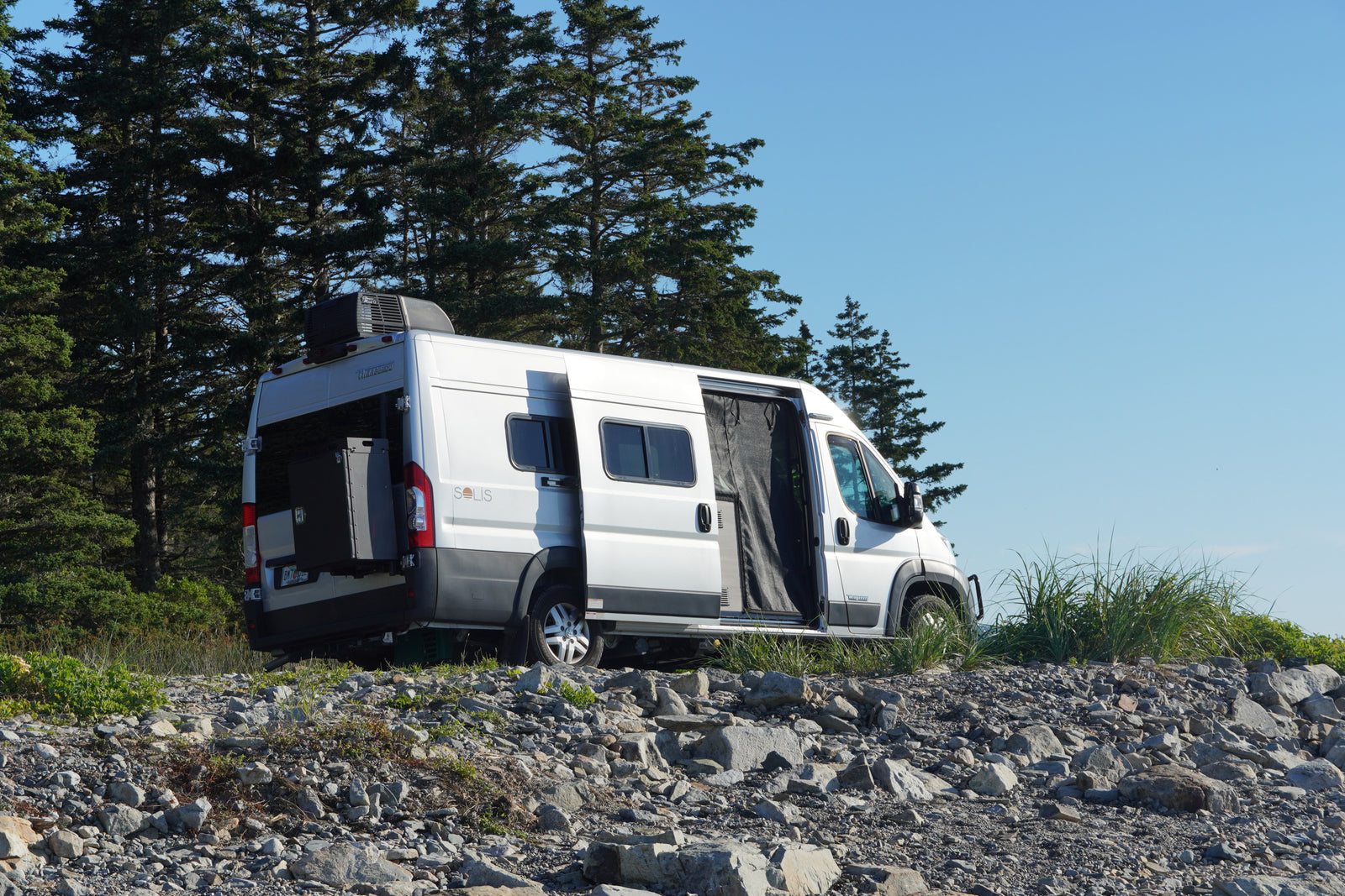 A silver Winnebago Solis RV rental camper van is parked on rocky terrain with doors open