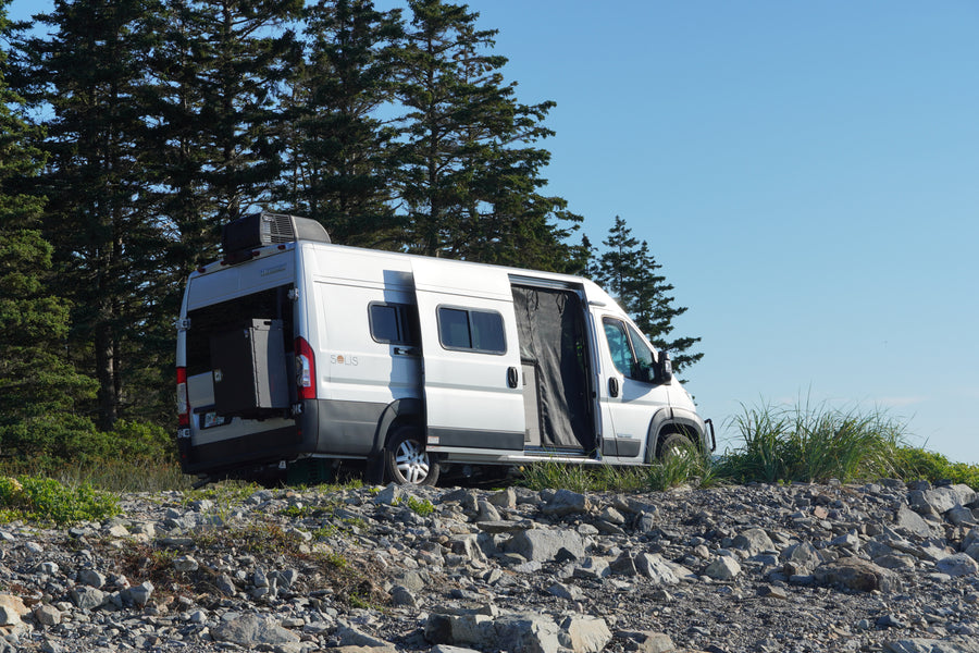 A silver Winnebago Solis RV rental camper van is parked on rocky terrain with doors open