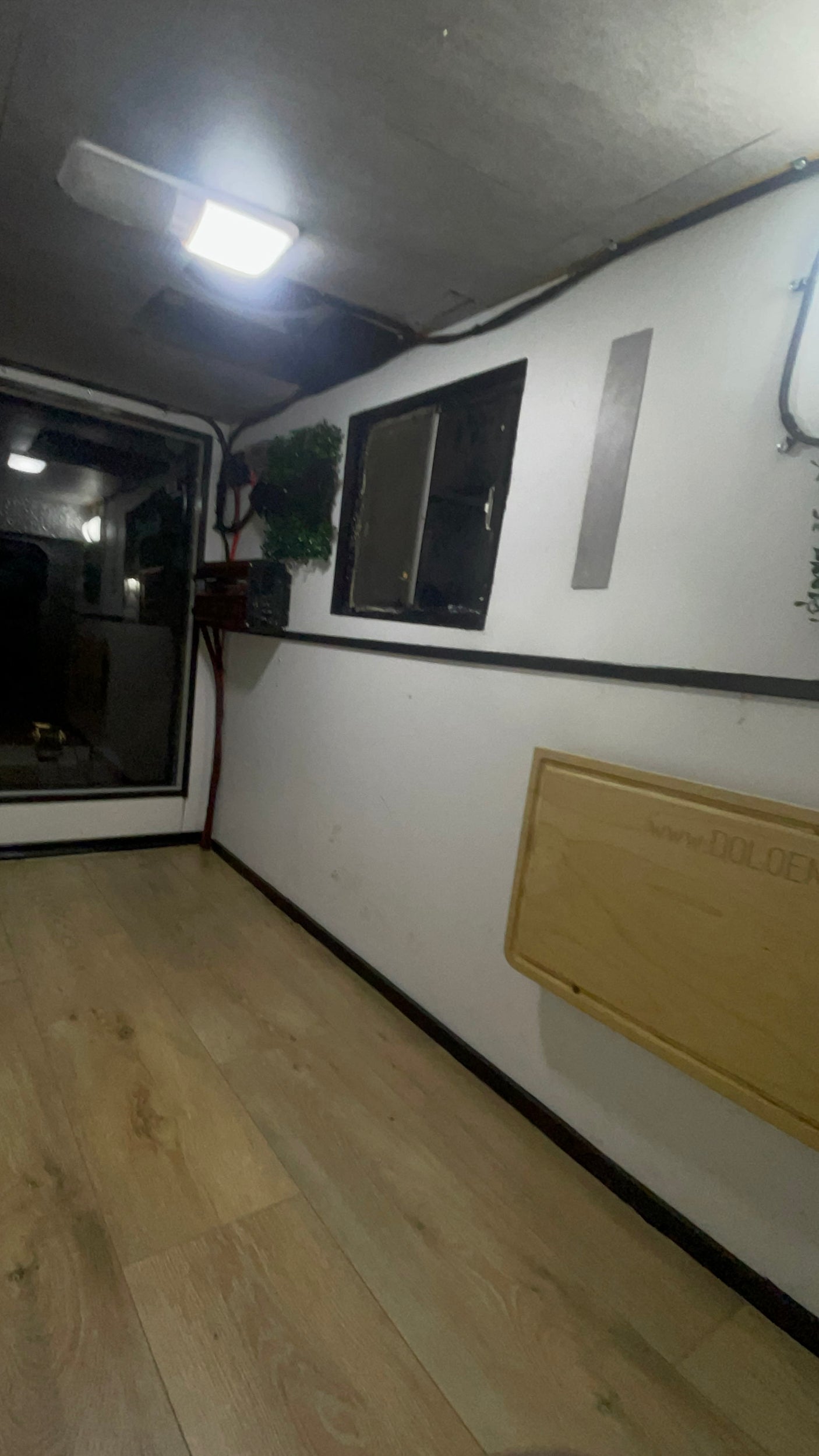 Bright RV rental interior with light wood flooring, white walls, ceiling light, and a small window. A fold-down table adds versatility.