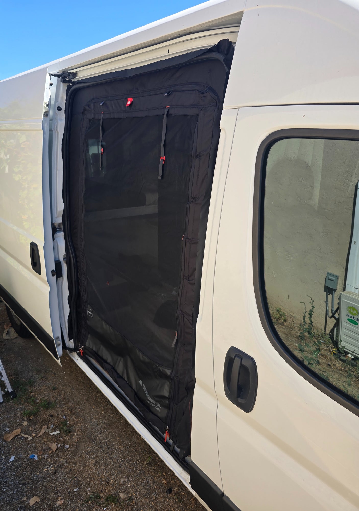 Side view of a white rv rental van with its sliding door open, showcasing a black mesh bug screen for airflow.