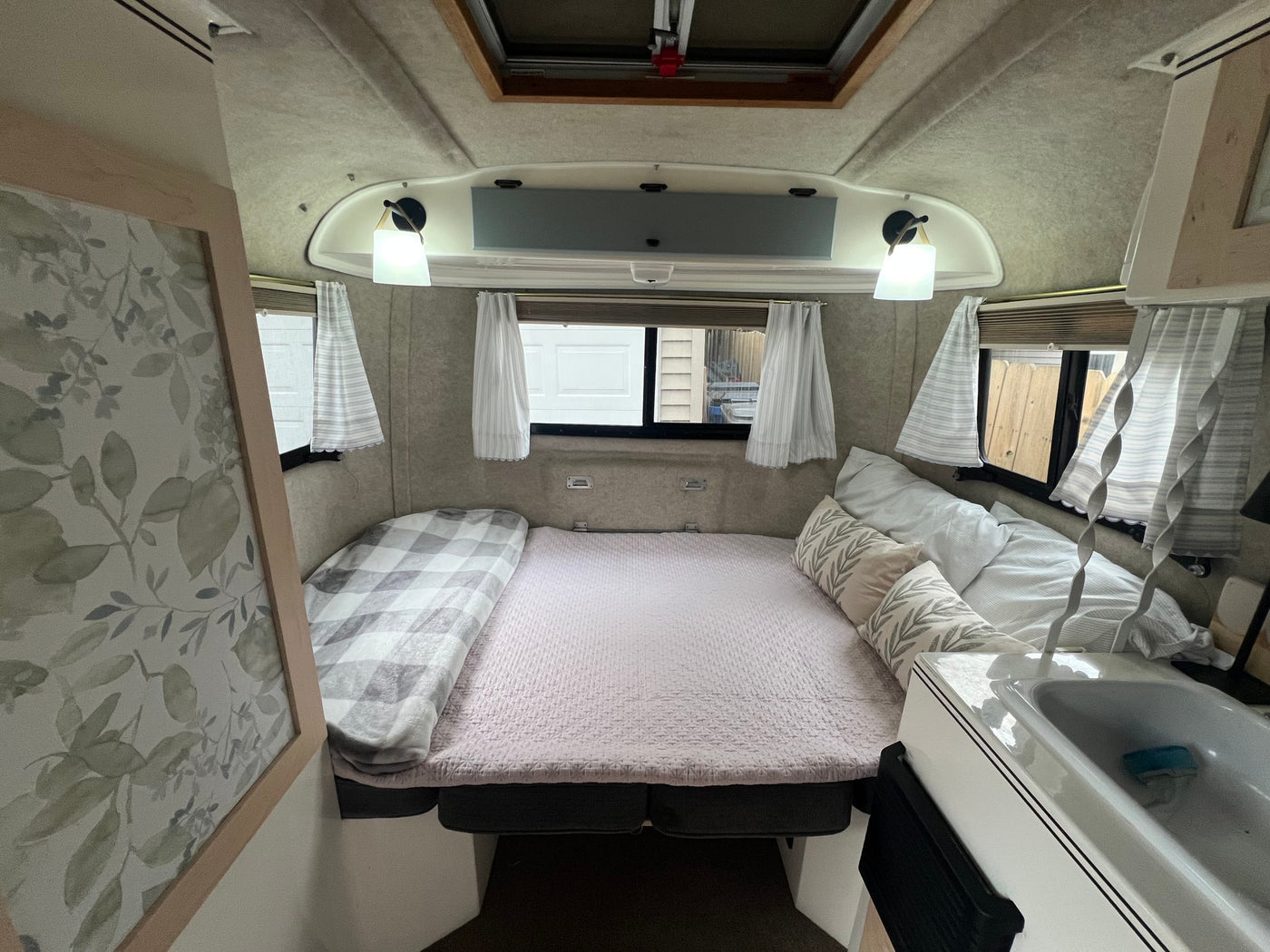 Explore this comfy RV rental bedroom area. Features a bed, leaf-patterned pillows, windows, and a compact sink. — photo 9