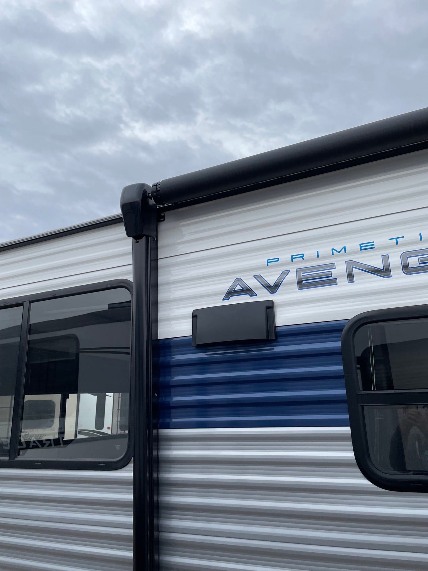 White & blue rv rental exterior: corrugated siding, dark windows, & black awning against a cloudy sky. Ready for travel. — photo 7