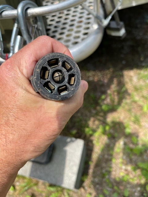 A hand holds a 7-pin RV trailer electrical plug, essential for rv rental and towing. Visually impaired: Round black connector.