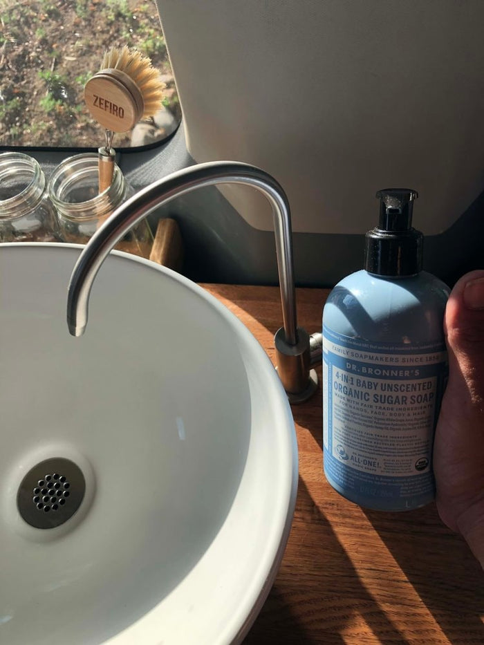 an adult and child relax on a cozy bed. Perfect family travel in a spacious camper van.|An RV rental's compact sink area: white bowl