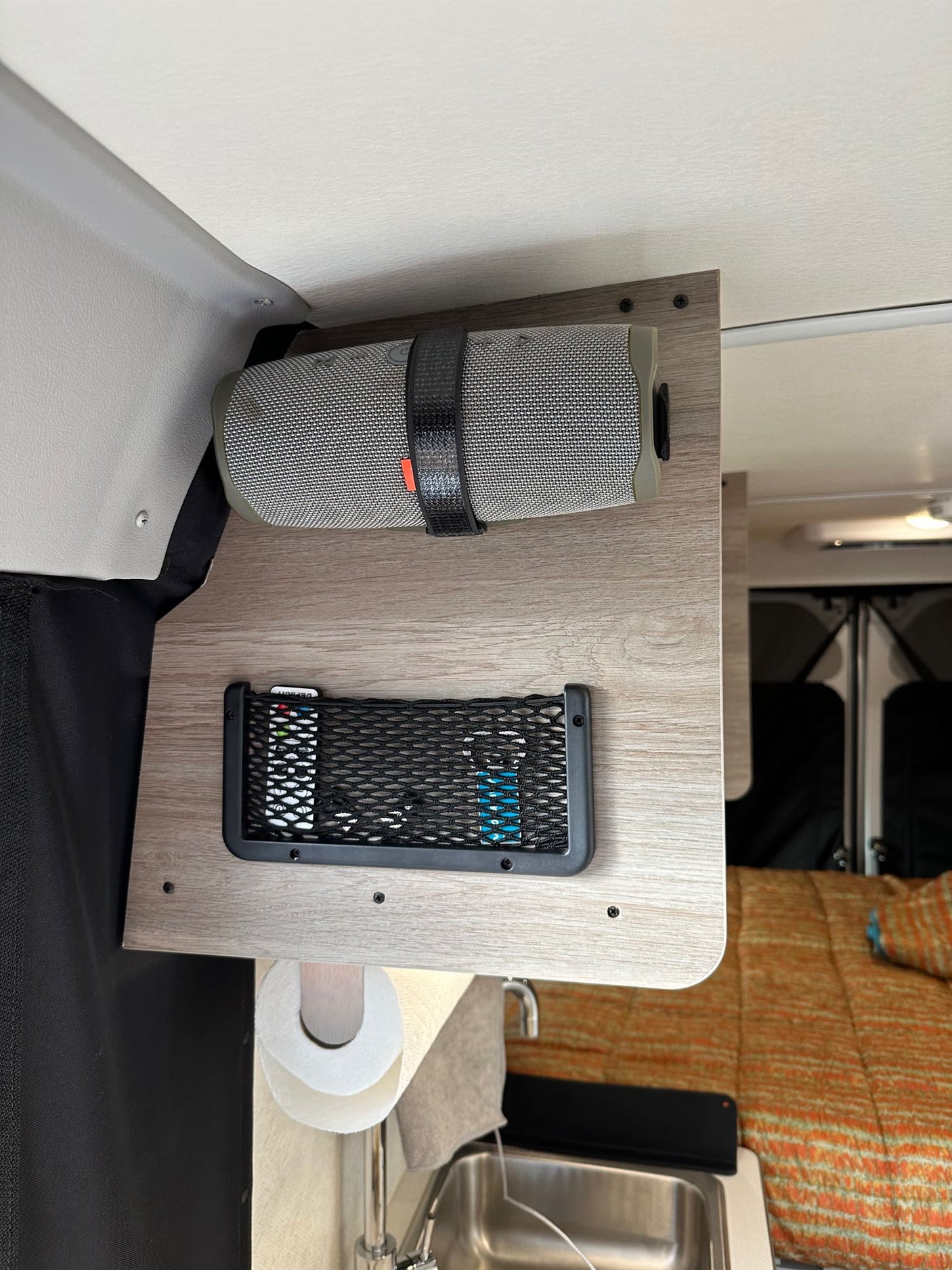 RV rental's compact living setup: overhead speaker, remotes in net, paper towels, & sink.