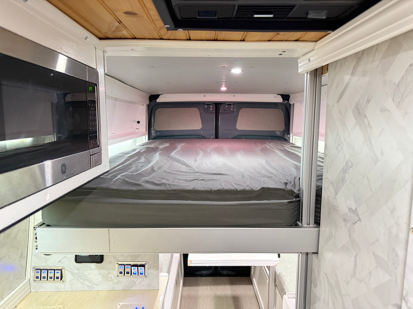 RV rental campervan interior with a cozy elevated bed, integrated microwave, and control panel. Perfect for van life.