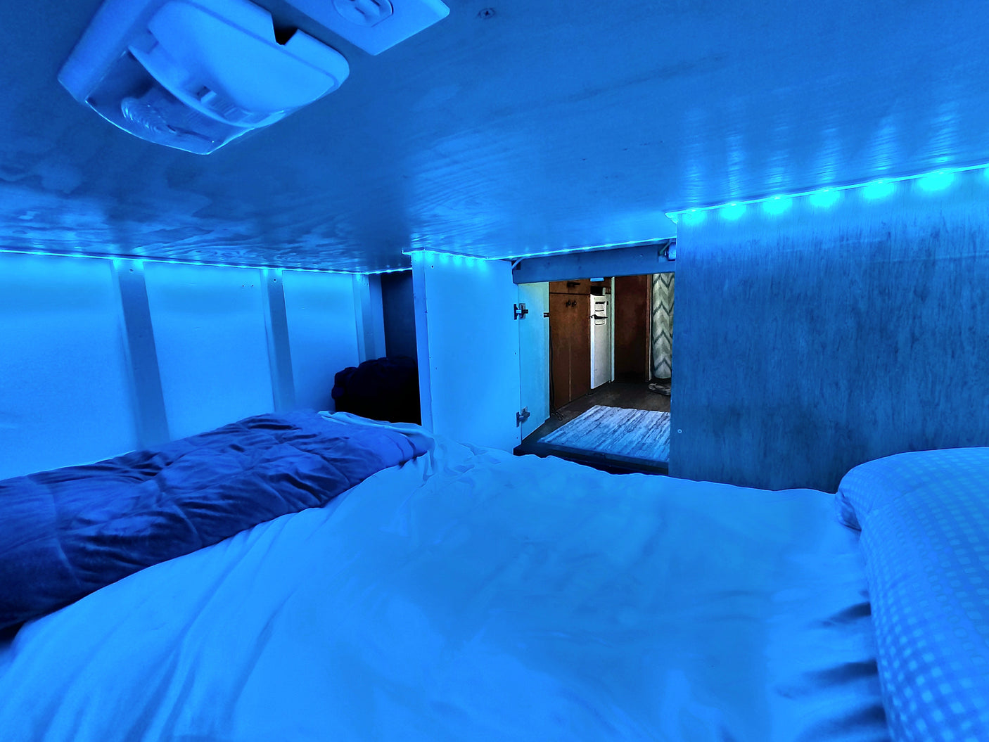 Cozy RV rental sleeping nook with blue LED strip lights illuminating the bed and interior.