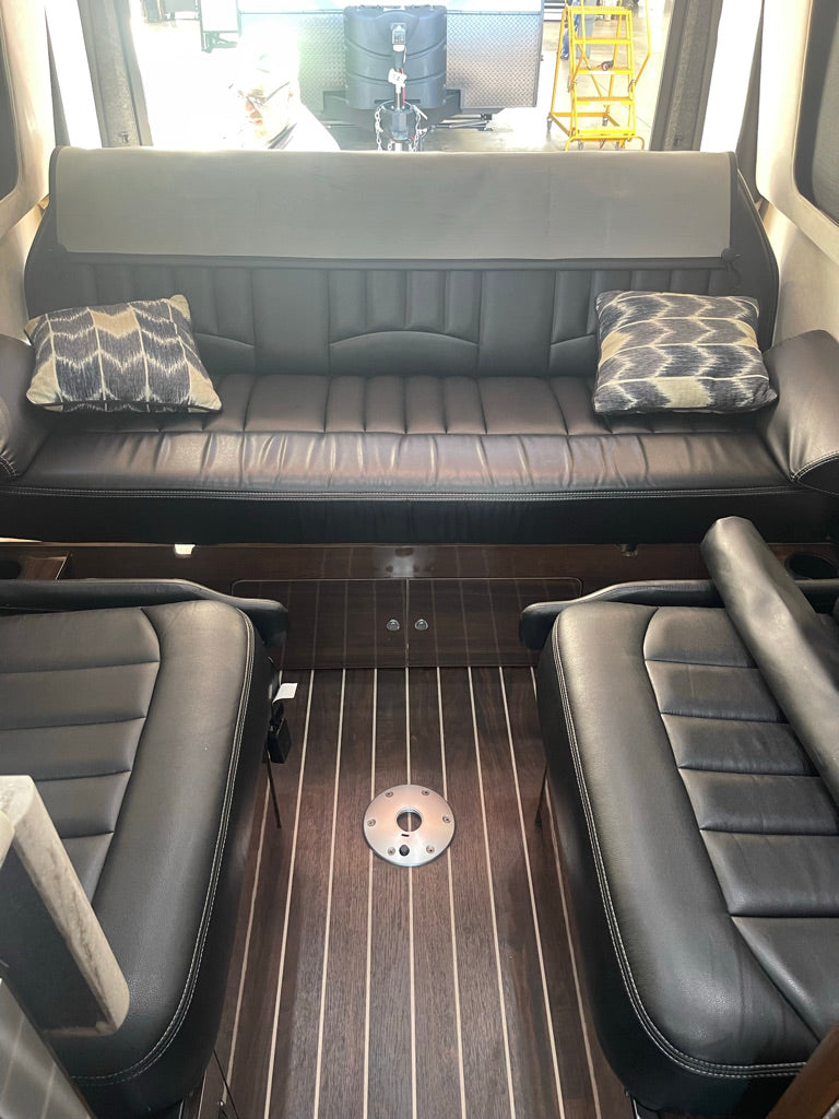 Spacious RV rental interior with comfortable black leather sofa, matching captain's chairs, and a sleek wood floor, ready for your road trip comfort.