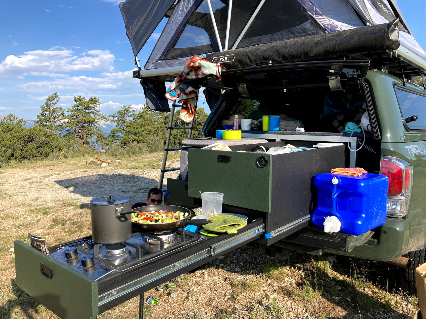 Green truck with pull-out kitchen & rooftop tent: cooking fresh veggies outdoors. Perfect for adventurous RV rental camping!