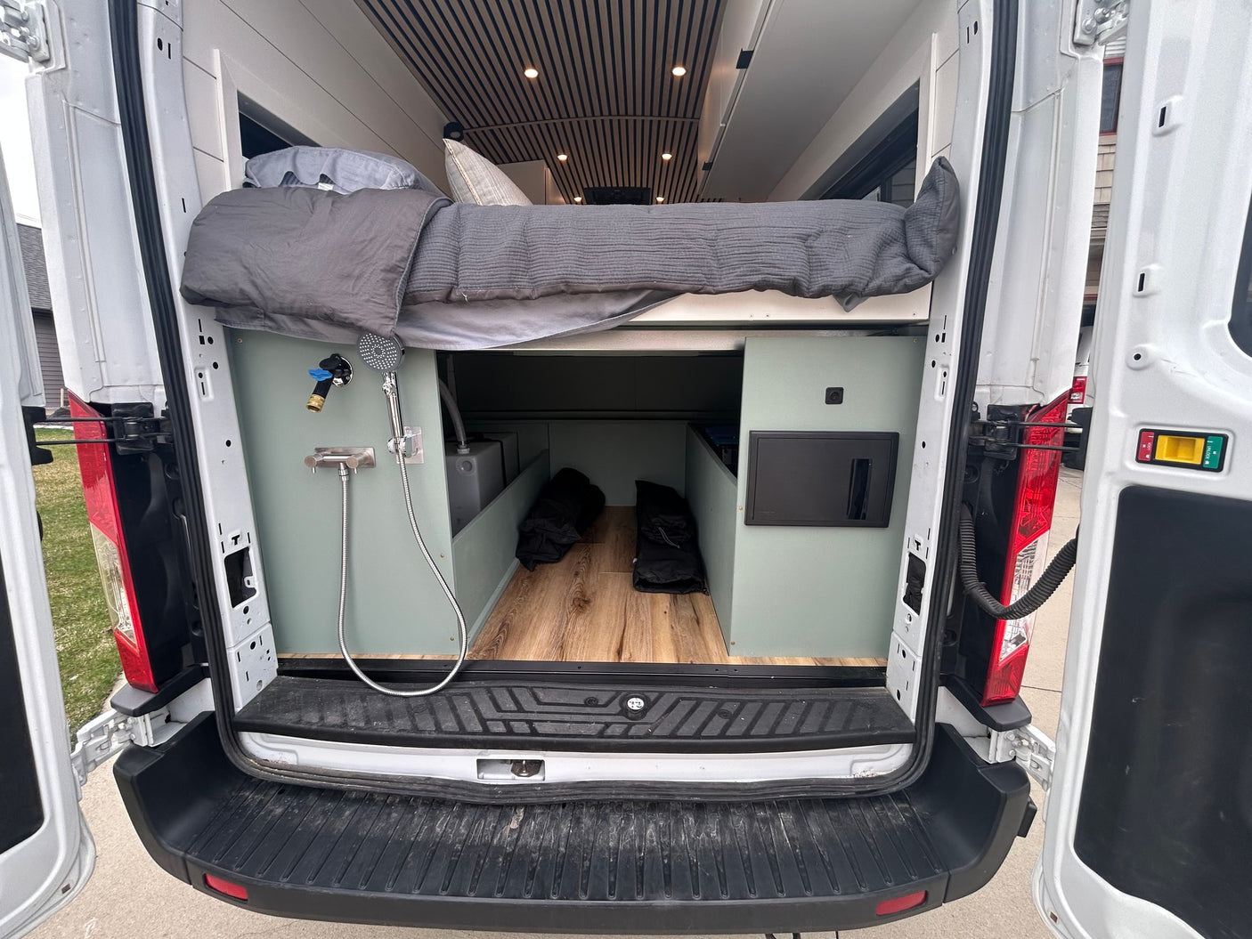RV rental camper van interior: rear view with raised bed, outdoor shower, under-bed storage, and electrical panel.
