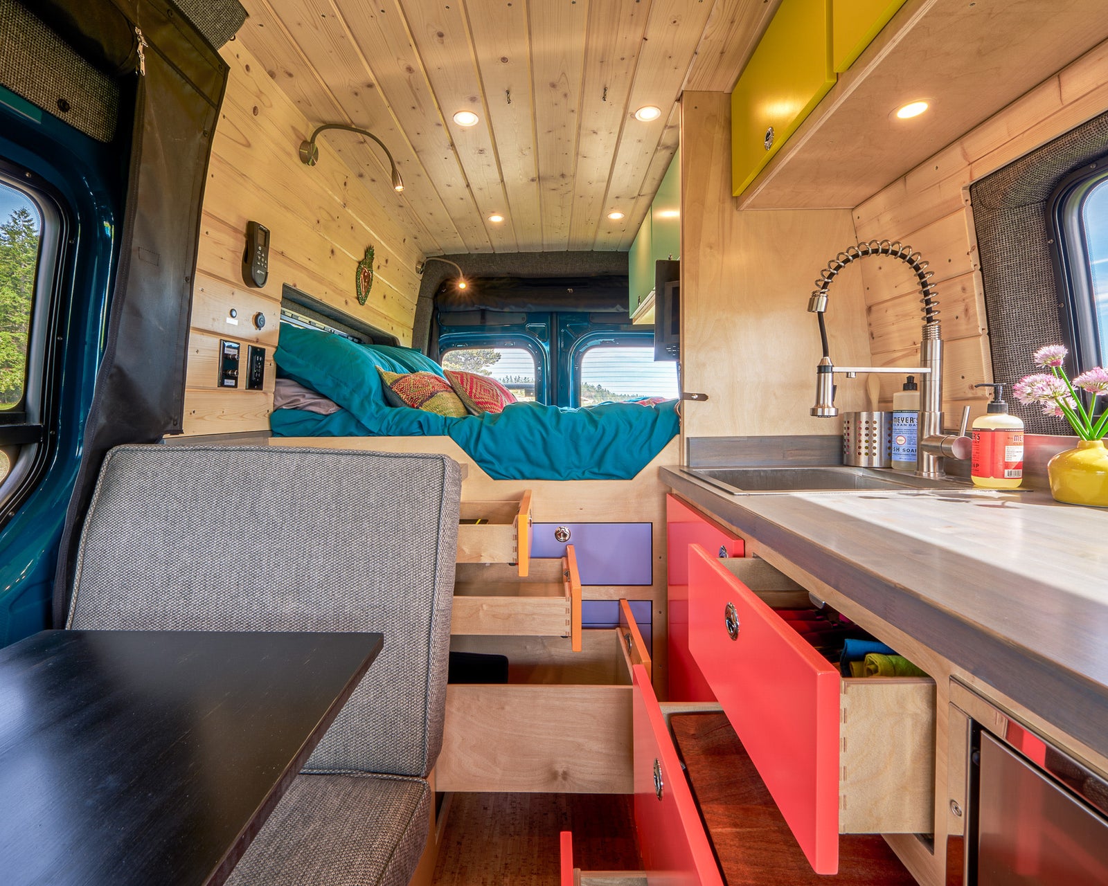 Colorful RV rental interior featuring a kitchen, bed area, and modular storage for a comfortable camper experience.