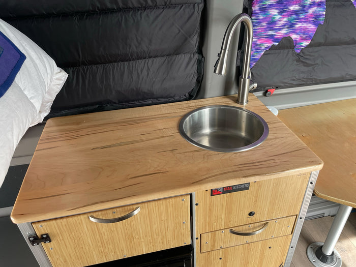 Inside an RV rental: a modern compact kitchen with a stainless sink, sleek faucet, and wooden counter.