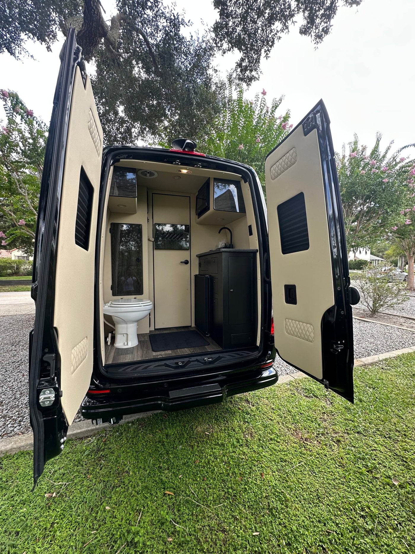 is parked on gravel by a path under trees.|Luxury black Mercedes-Benz Sprinter van — photo 4
