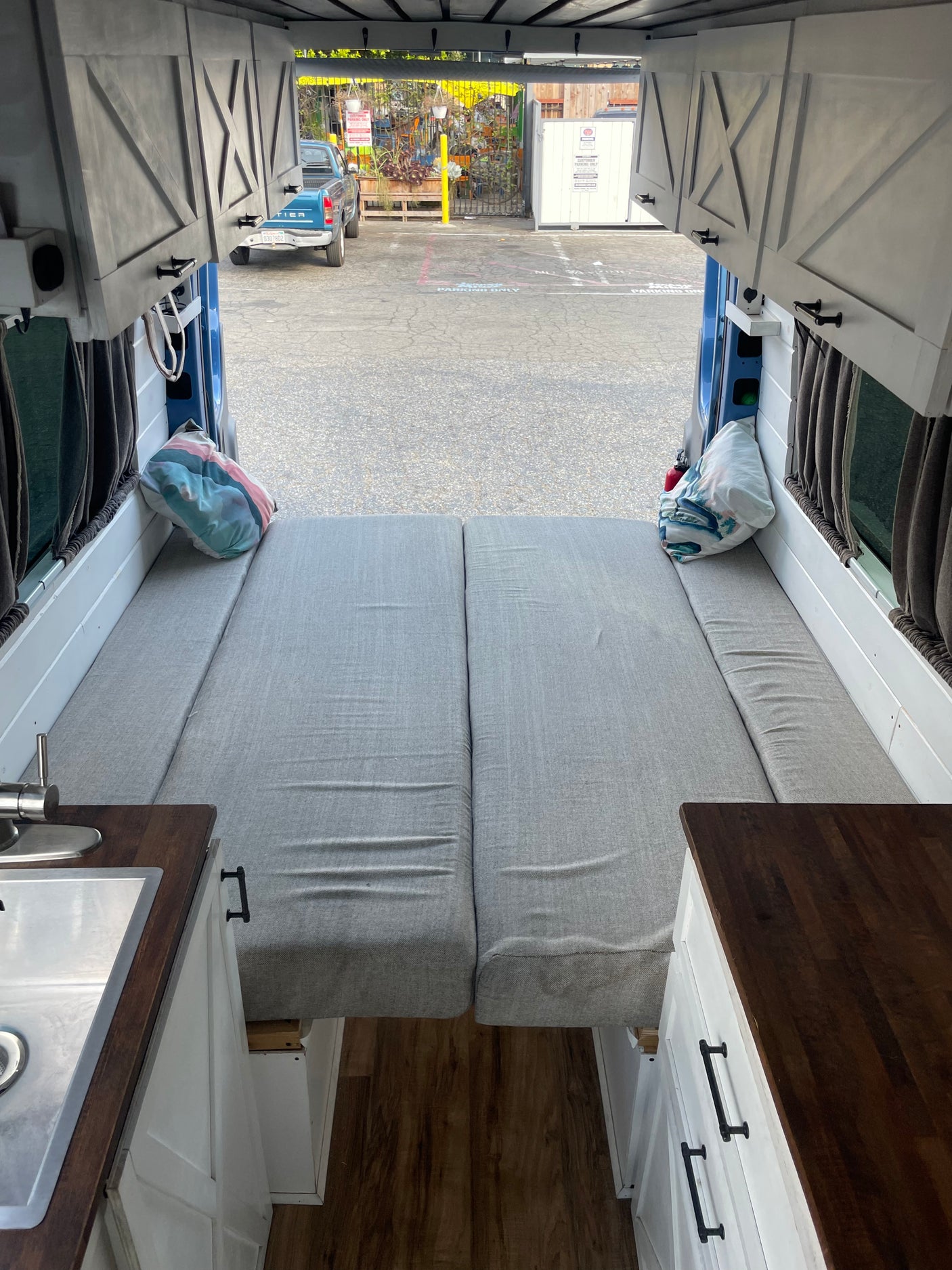 RV rental interior: comfy grey bed, kitchenette, and storage cabinets in a custom camper van. View out back doors.