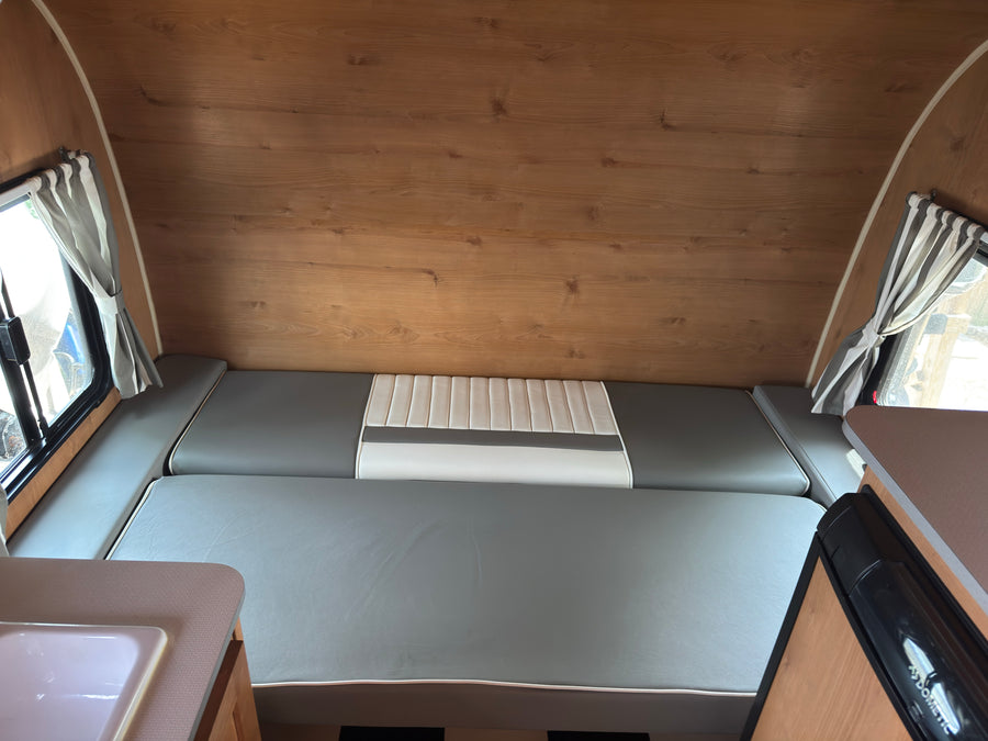 RV rental interior: wood-paneled walls, gray & white convertible bed/seating, striped curtains, sink, & Dometic fridge.