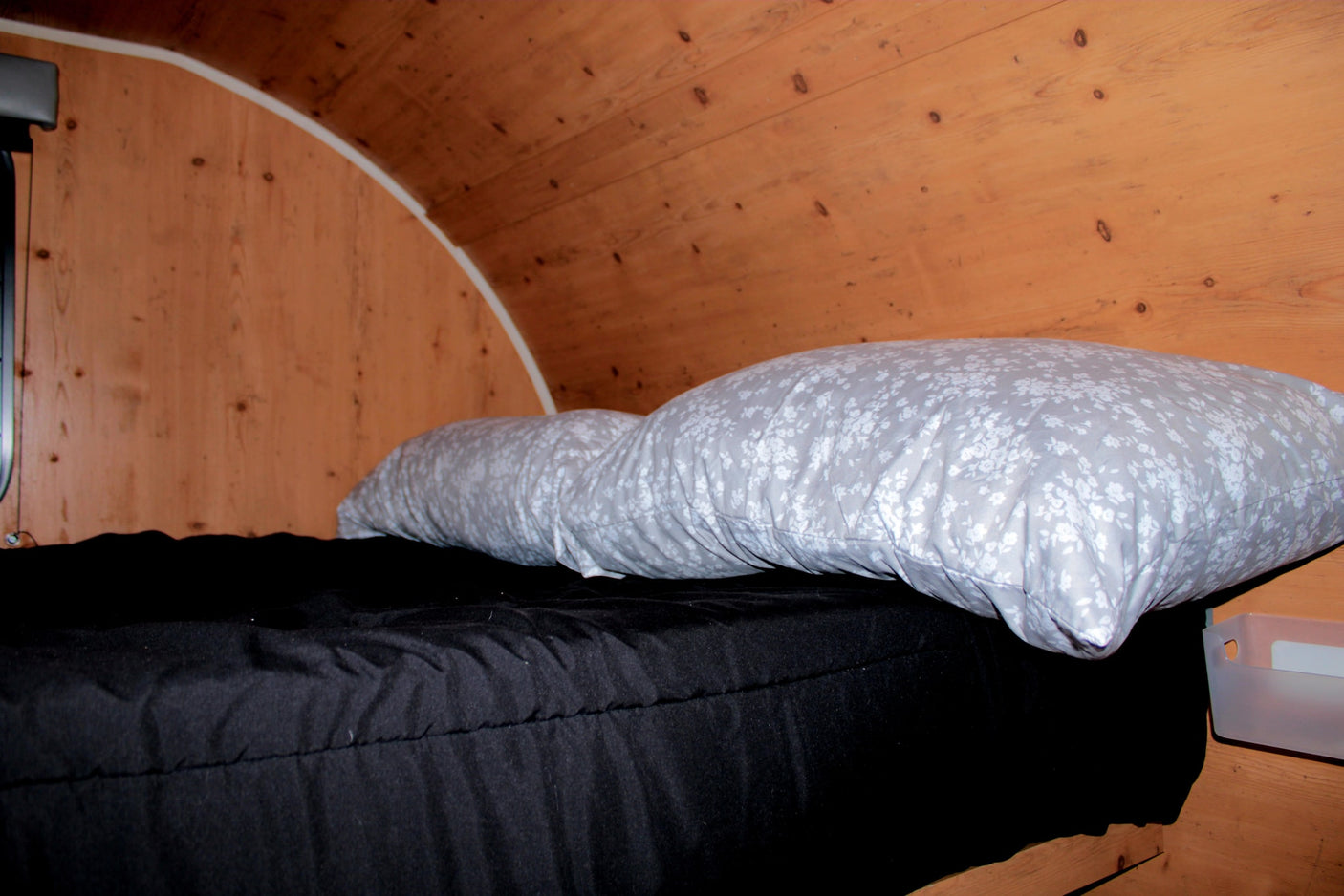 This rv rental features a cozy sleeping area with dark bedding, floral pillows, and a curved wooden ceiling.