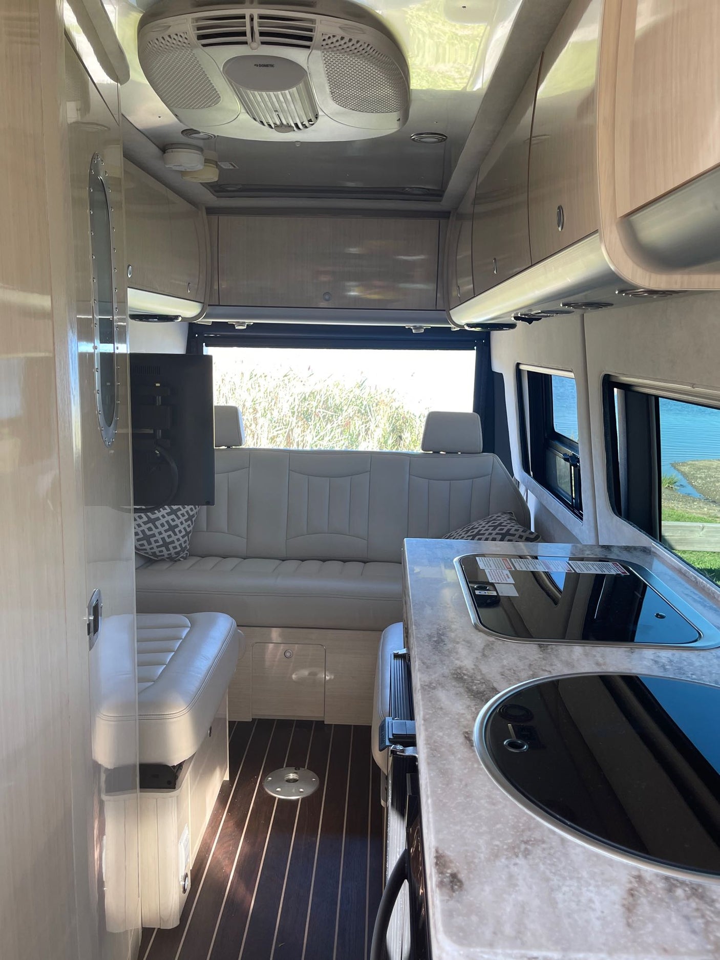 sunlit forest. Perfect for nature adventures.|RV rental camper van with bike rack & gravel bike for adventure.|Black Airstream Interstate rv rental with awning. Two Tommy Bahama chairs & mat by a lake. Relaxing outdoor setup.|Inside this spacious RV rental: plush cream seats