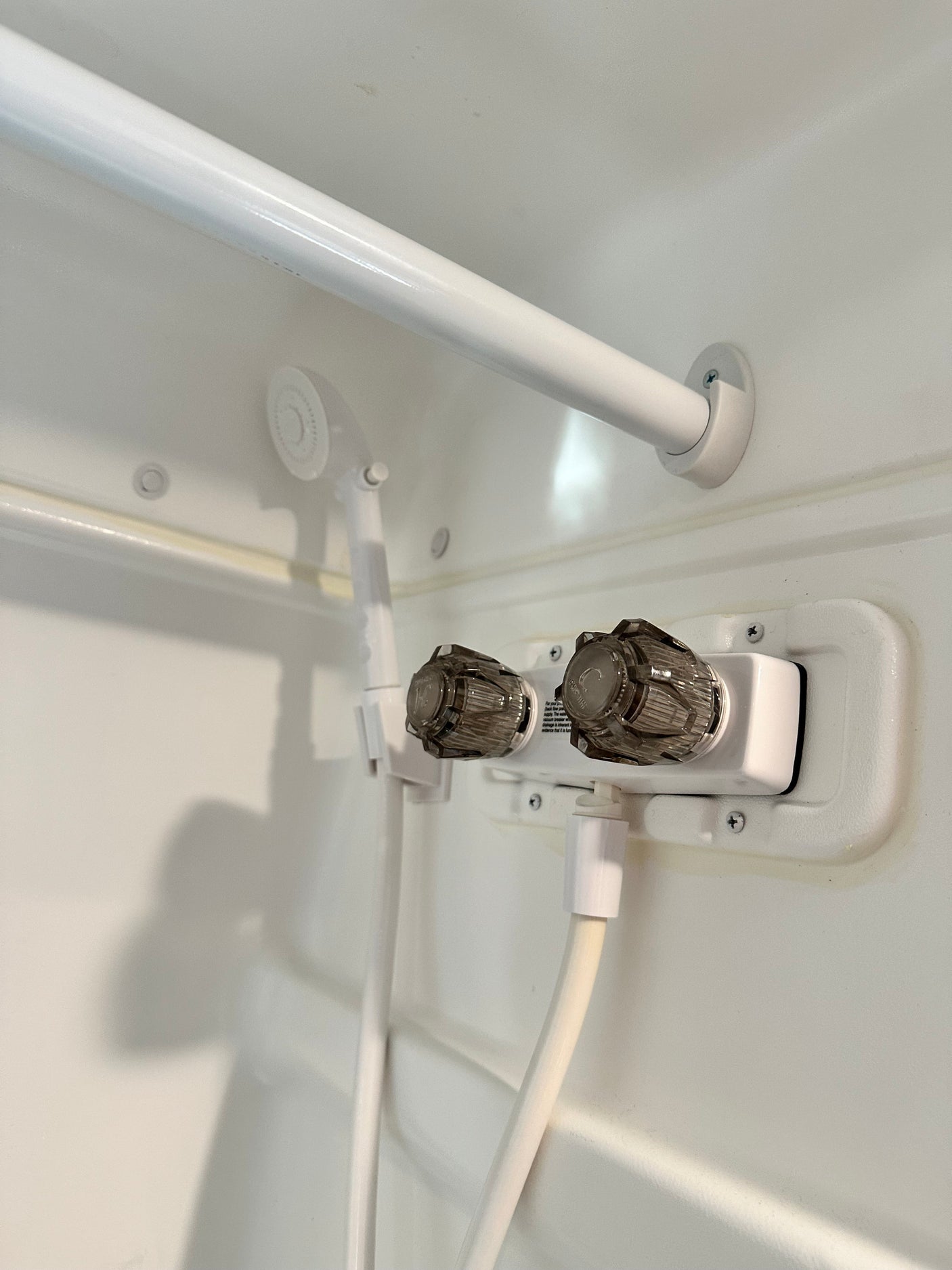 An RV rental's compact shower interior, featuring white walls, a two-handle faucet, and a handheld shower head.