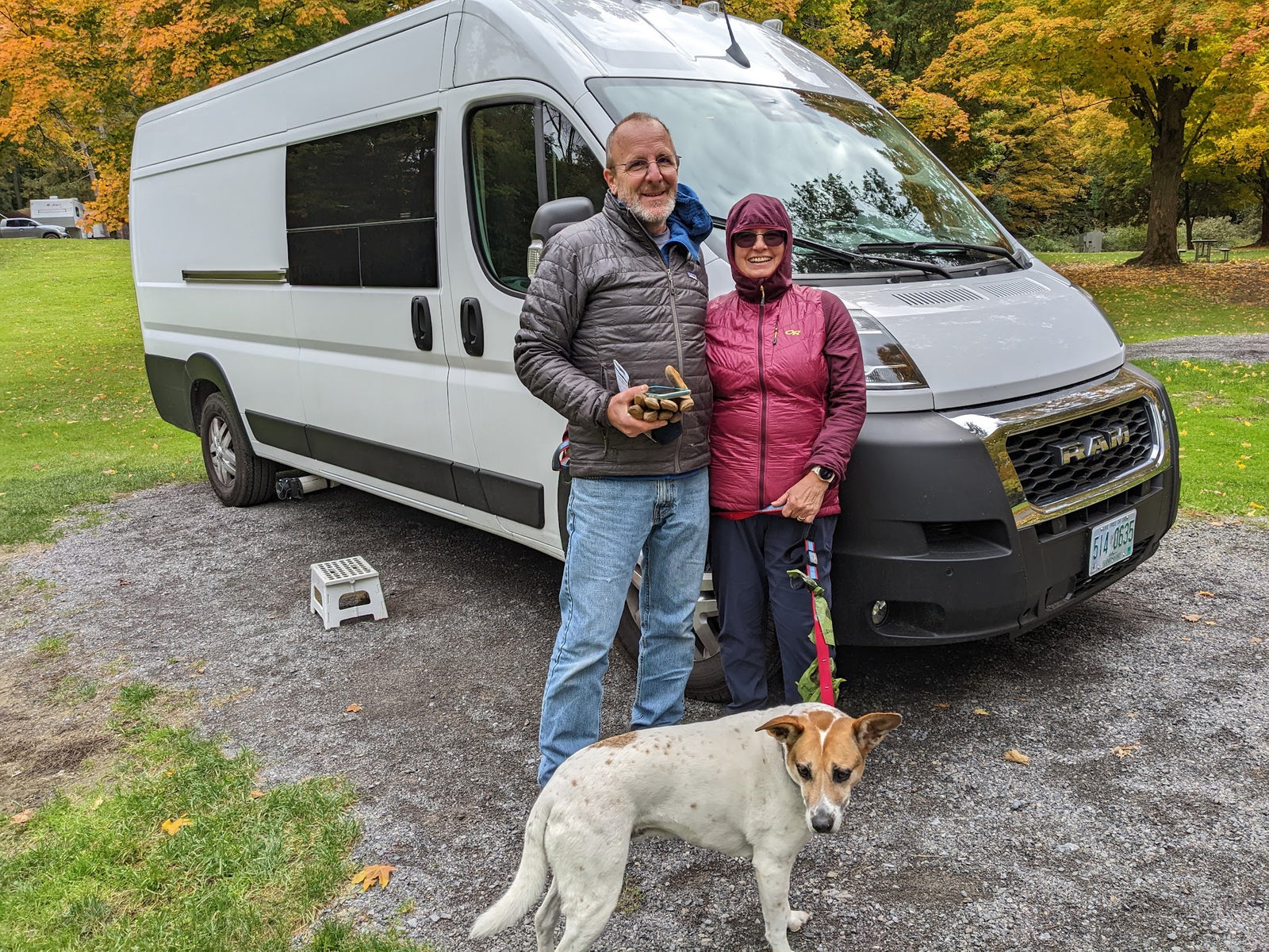 Happy couple and their dog enjoying an RV rental van at a scenic fall campsite. Perfect for adventurers!