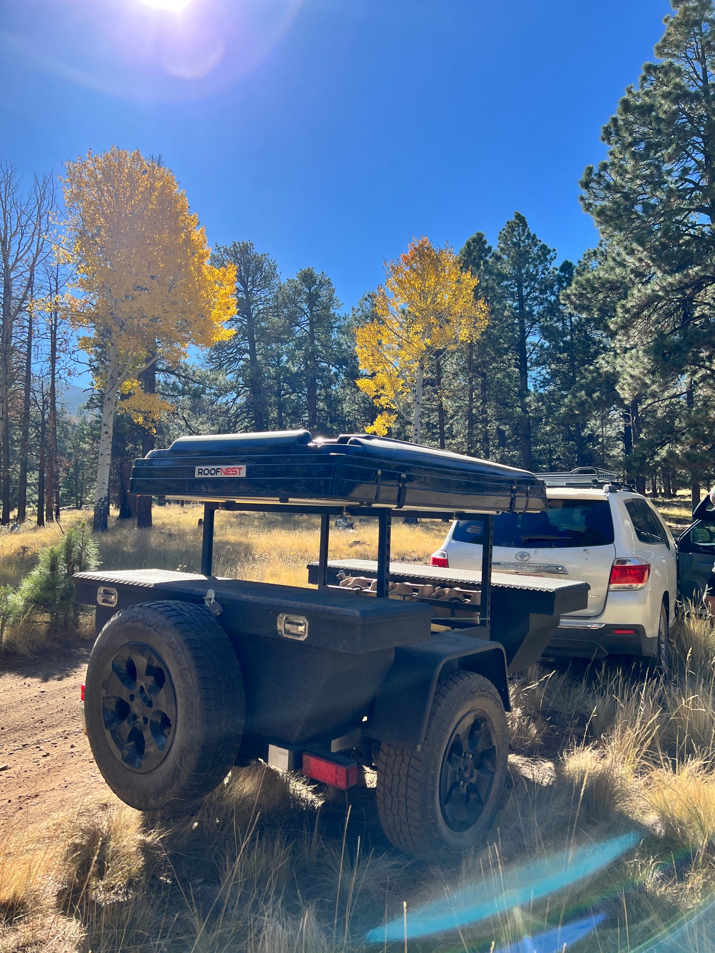 An adventure-ready trailer with rooftop tent (like an rv rental) and SUV parked amidst vibrant fall foliage for camping.