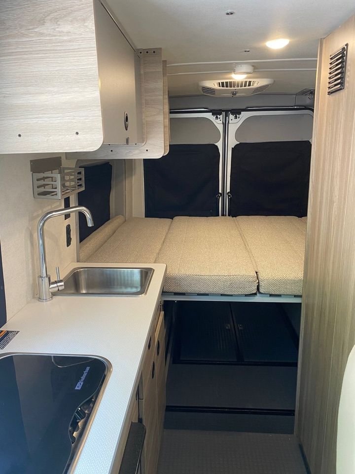 Spacious RV rental interior with a compact kitchen, sink, stovetop, cozy bed, and overhead storage for your travels.