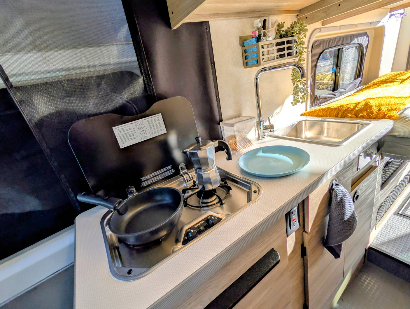 This RV rental's efficient kitchenette includes a stovetop, sink, and tools like a moka pot and pan, perfect for travel cooking.
