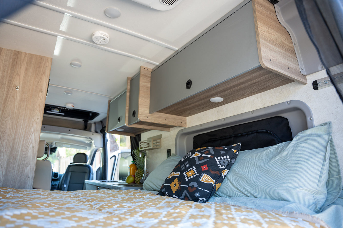 Step inside this cozy RV rental's interior, featuring a comfortable bed, overhead cabinets, and a compact kitchen.