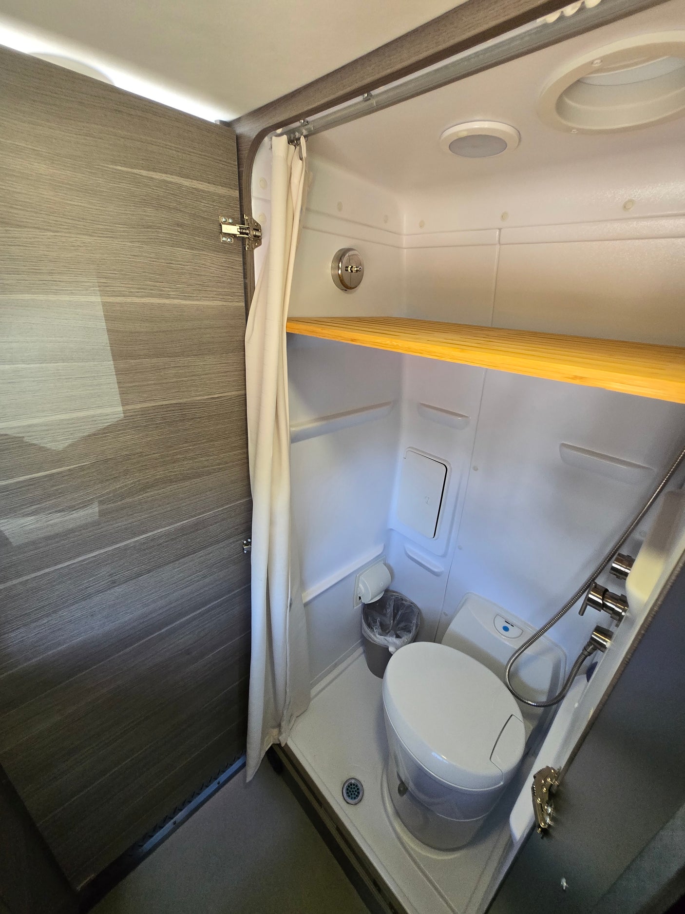 RV rental's compact wet bath featuring a toilet, shower, and practical wooden shelf.