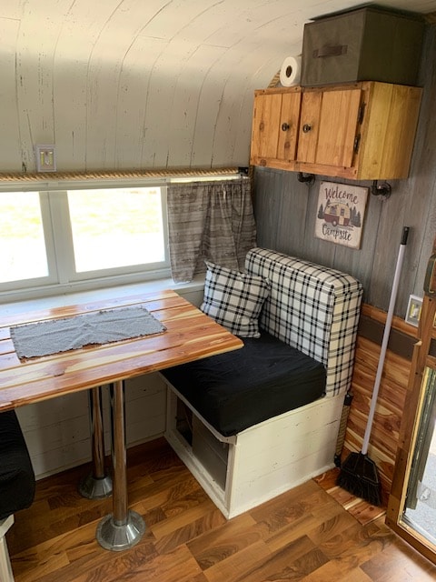 Inviting rv rental interior. Features a cozy plaid bench, wooden table, storage, and homey camp decor.