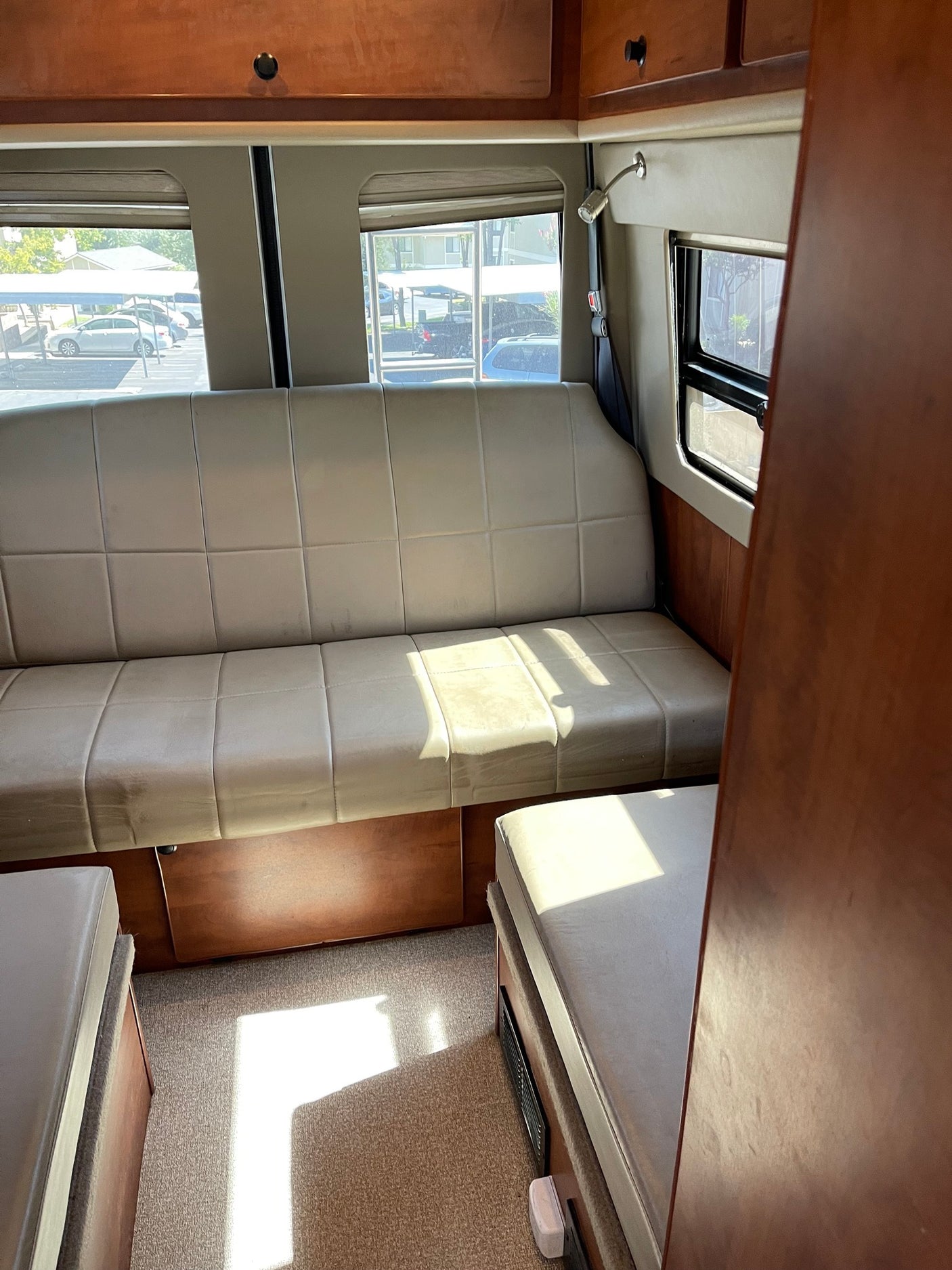 Inside an RV rental: light-colored bench seating, wood cabinets, and large windows revealing the outside.