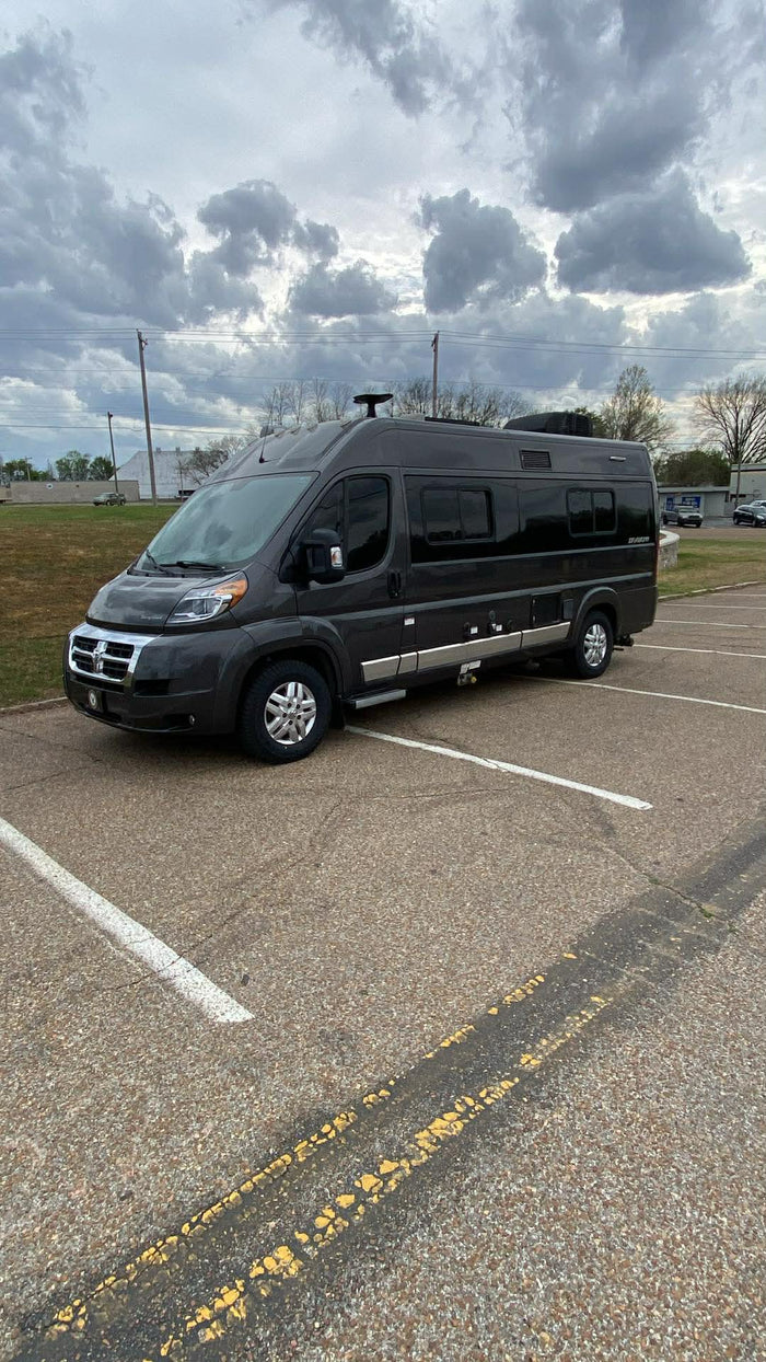 and colorful flowers are visible.|Side view of a dark gray Class B RV (camper van)