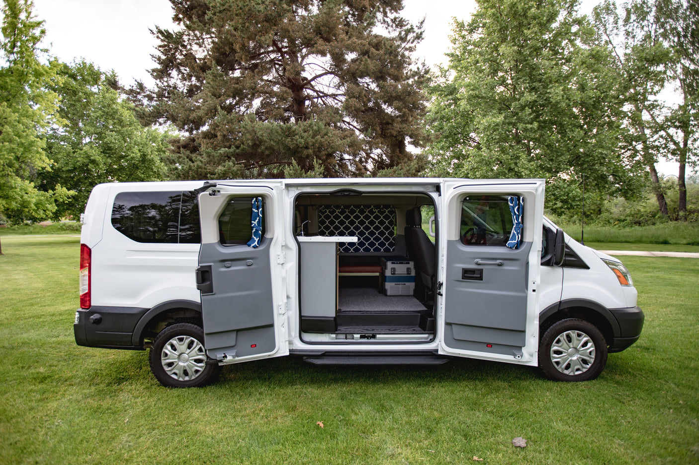 This white camper van, ideal for rv rental, reveals its custom interior with opened side doors on a grassy field.