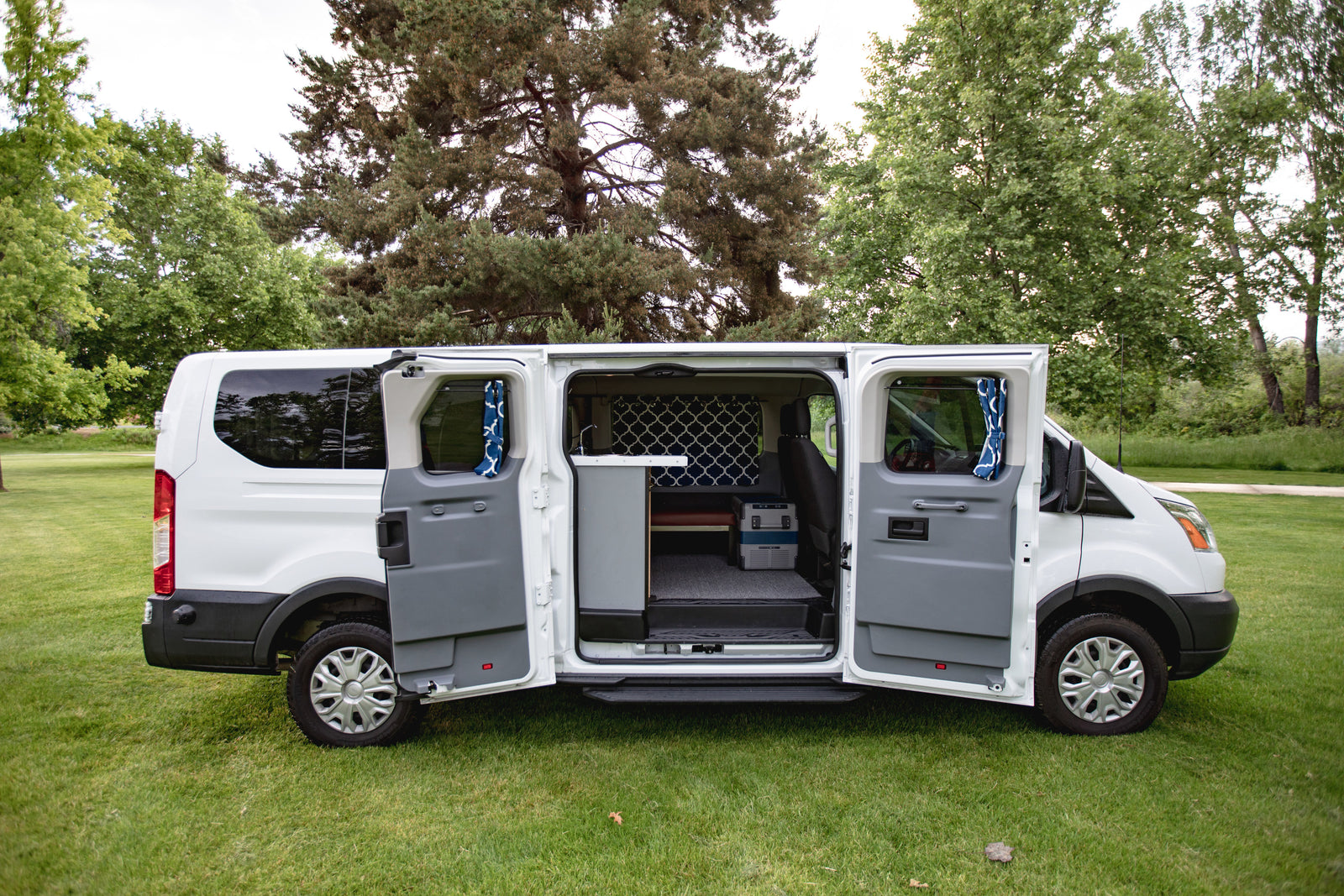 This white camper van, ideal for rv rental, reveals its custom interior with opened side doors on a grassy field.