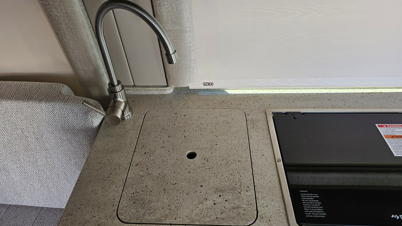RV rental interior: compact kitchen area with gooseneck faucet, covered sink, and stovetop on a modern countertop.