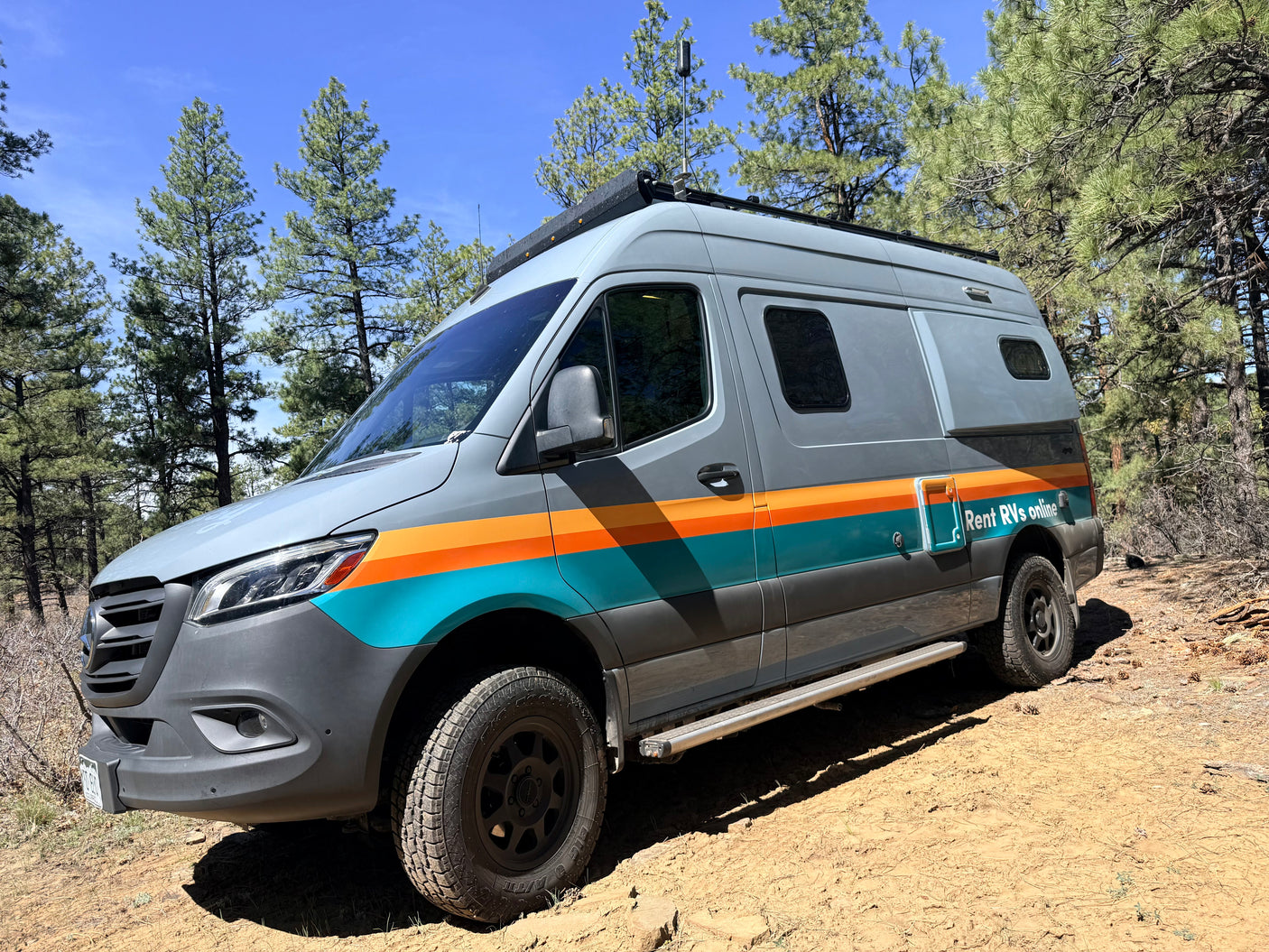 This gray Mercedes Sprinter RV rental, with "Rent RVs online" text, is ready for off-road adventure among pine trees.
