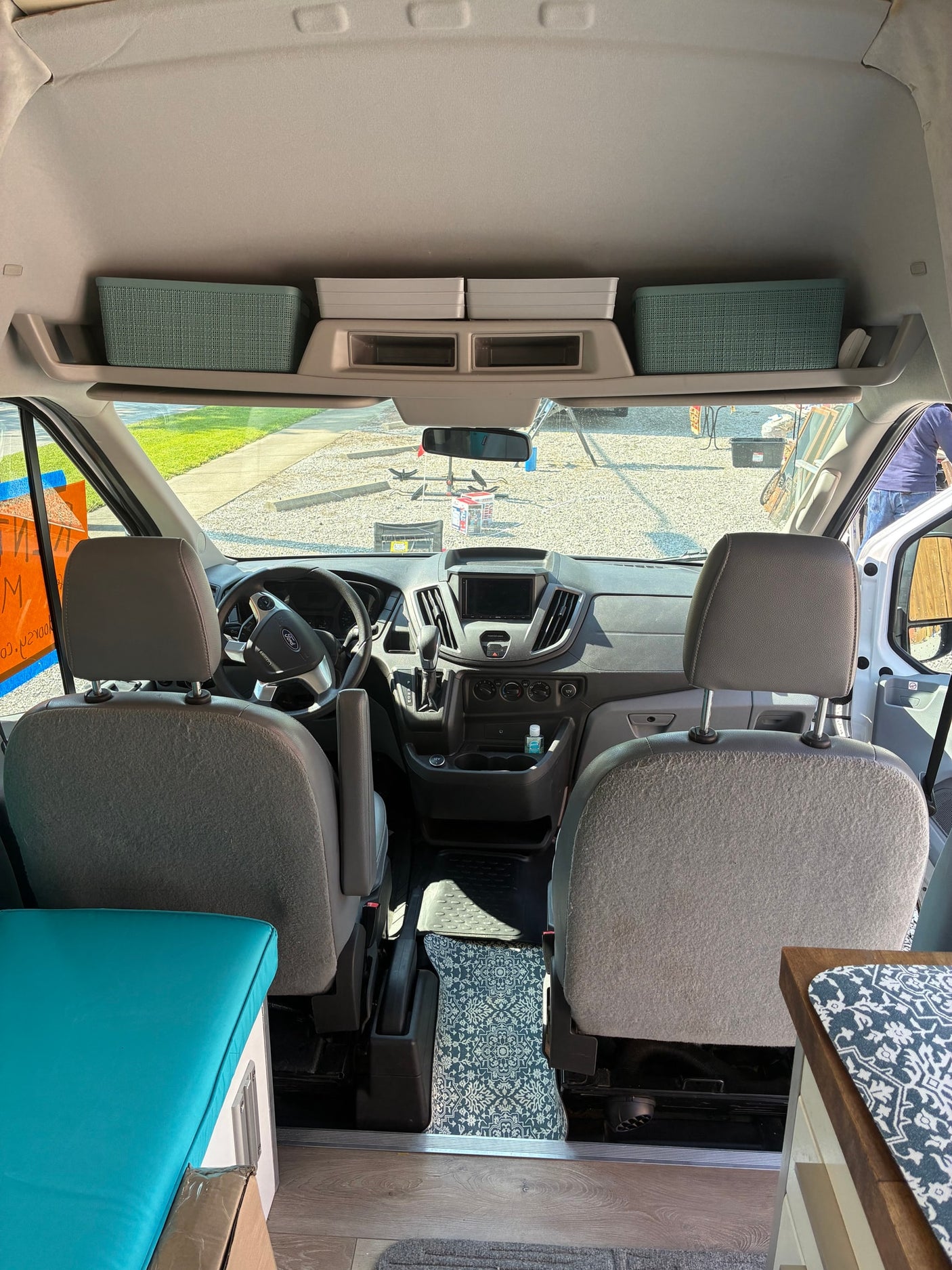 Inside this RV rental camper van, see the front seats, dashboard, and overhead storage bins from the living area.