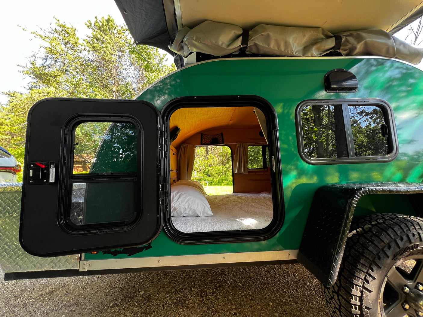 Green teardrop RV rental with open door revealing a cozy bed inside. Ideal for compact camping trips.