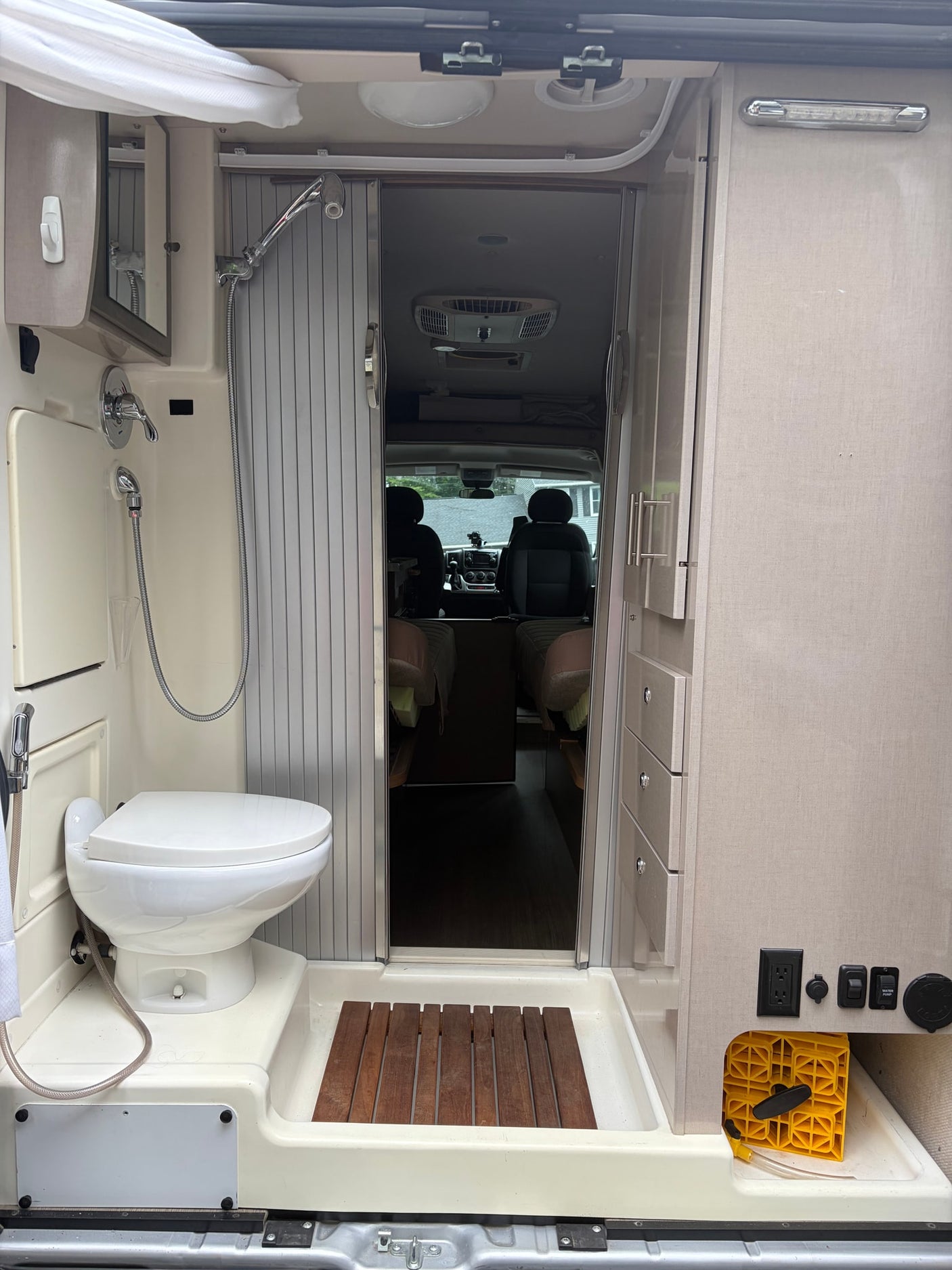 with an extended awning and open side door revealing its furnished interior.|Silver RV rental with extended awning & open side door parked at a house