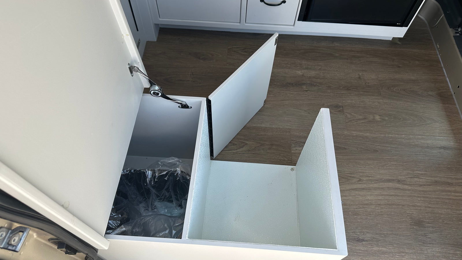 RV rental interior with a clever, pull-out trash bin and additional storage space in white cabinetry, ideal for travel.