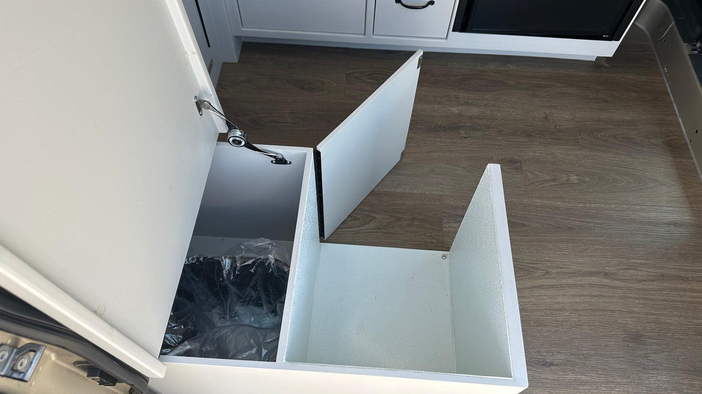 RV rental interior with a clever, pull-out trash bin and additional storage space in white cabinetry, ideal for travel.