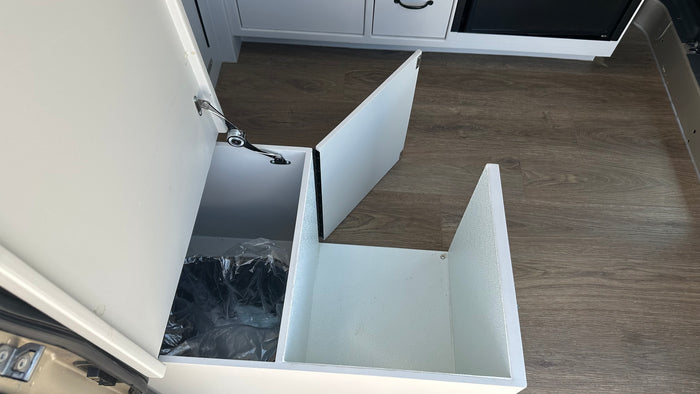 RV rental interior with a clever, pull-out trash bin and additional storage space in white cabinetry, ideal for travel.