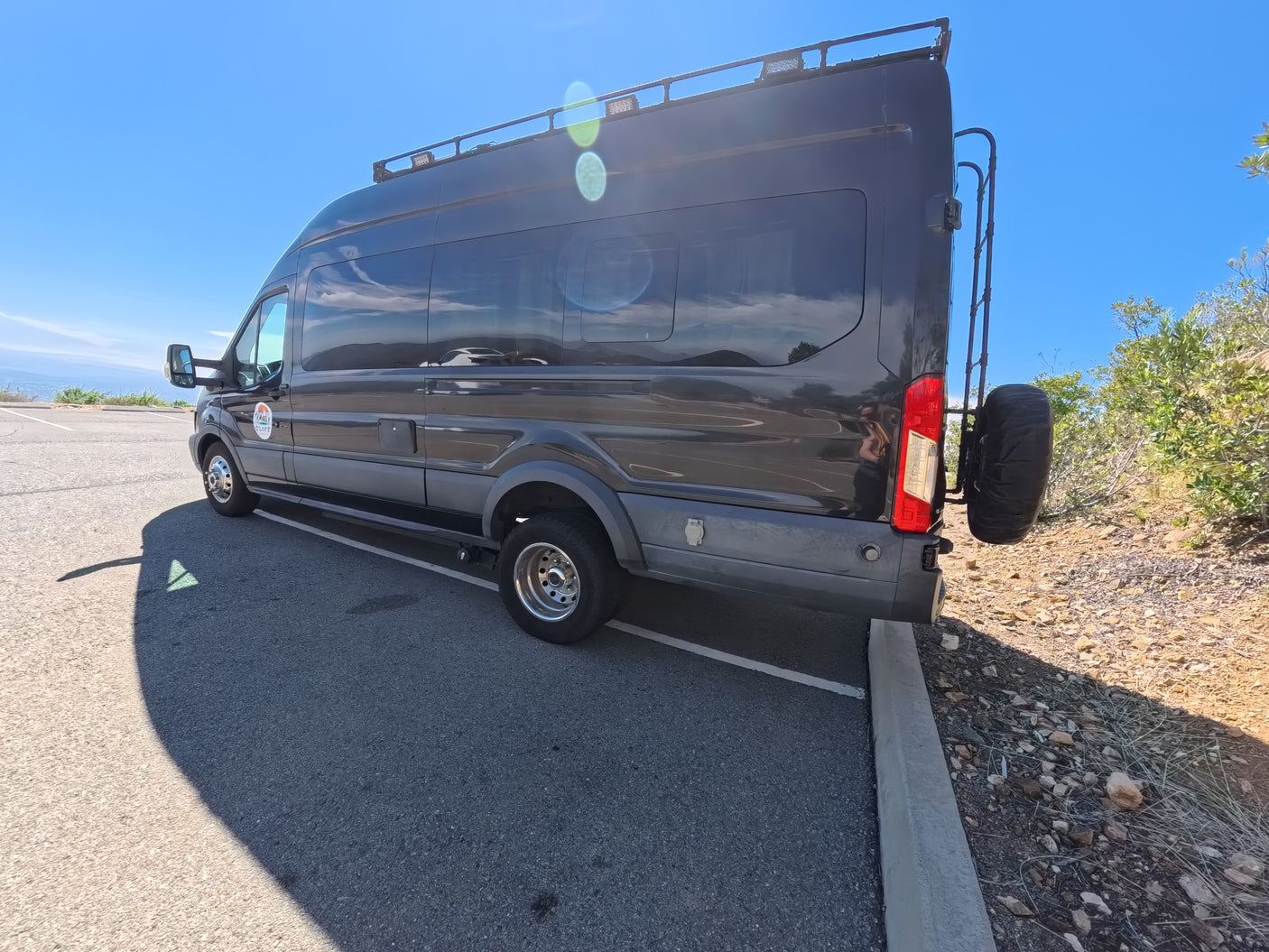 Dark gray RV rental van, with a roof rack & rear spare tire, parked for outdoor adventure.
