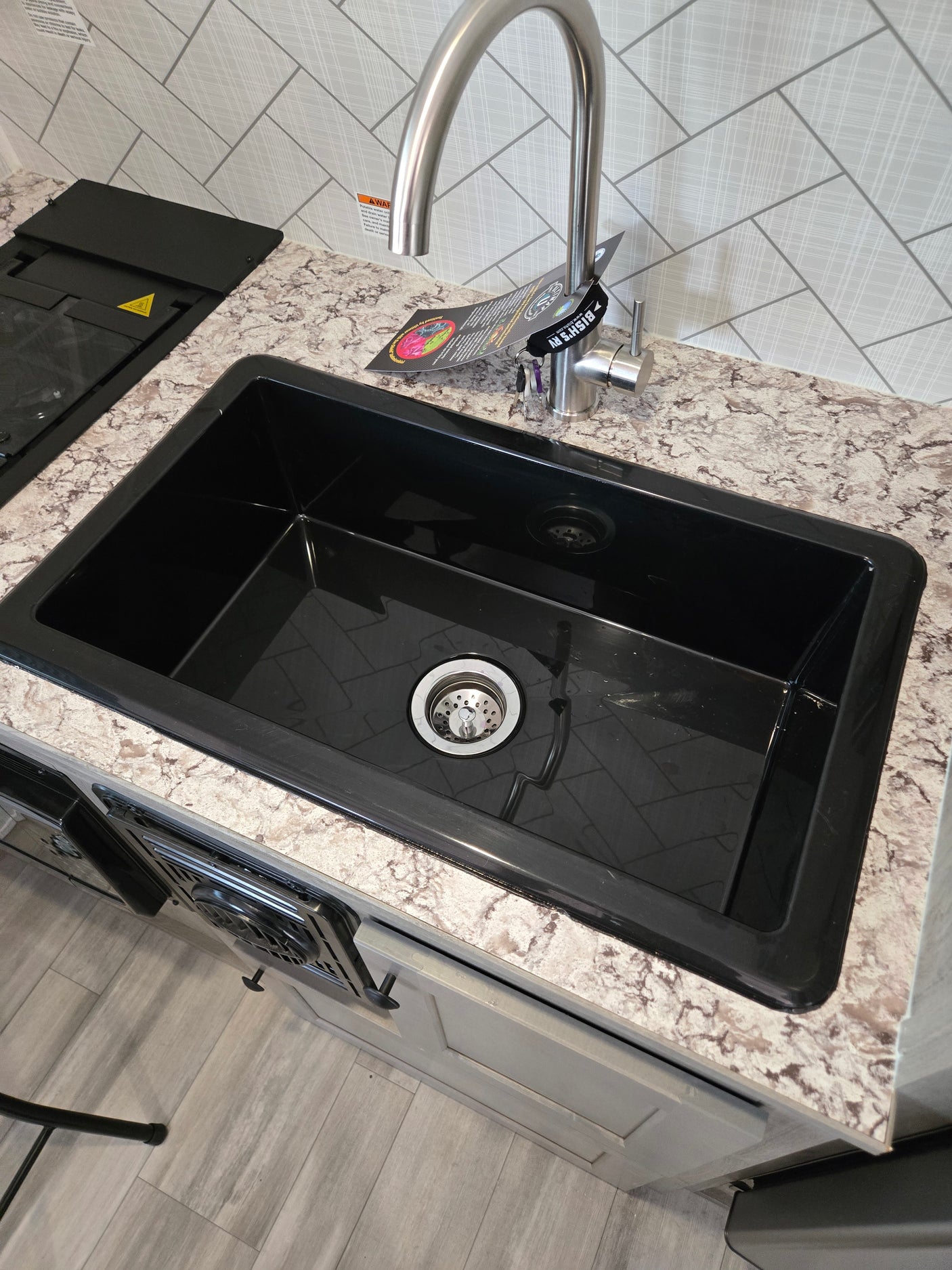 Sleek RV rental kitchen featuring a black sink, brushed stainless faucet, speckled counter, and herringbone backsplash. Stove visible.