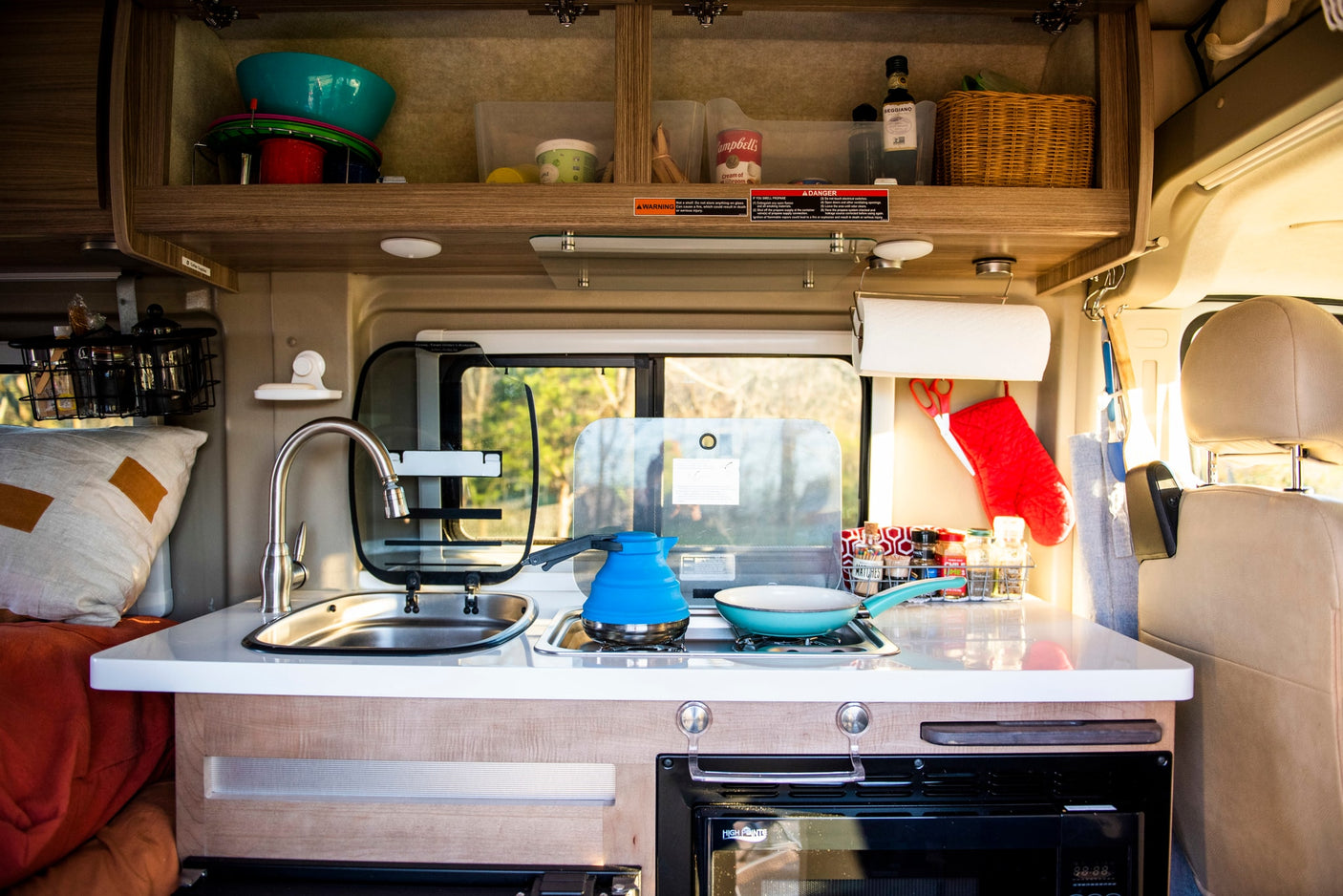 Well-equipped rv rental kitchen in a camper van, showing a sink, stove, and organized overhead storage for cooking supplies.