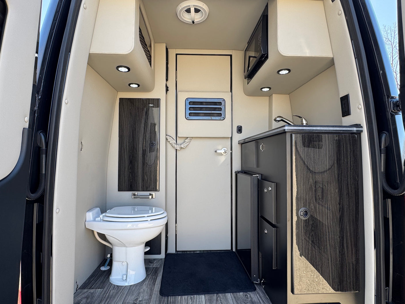 Explore this RV rental's well-equipped interior: a compact kitchen with sink/microwave, toilet, and storage inside this camper van.