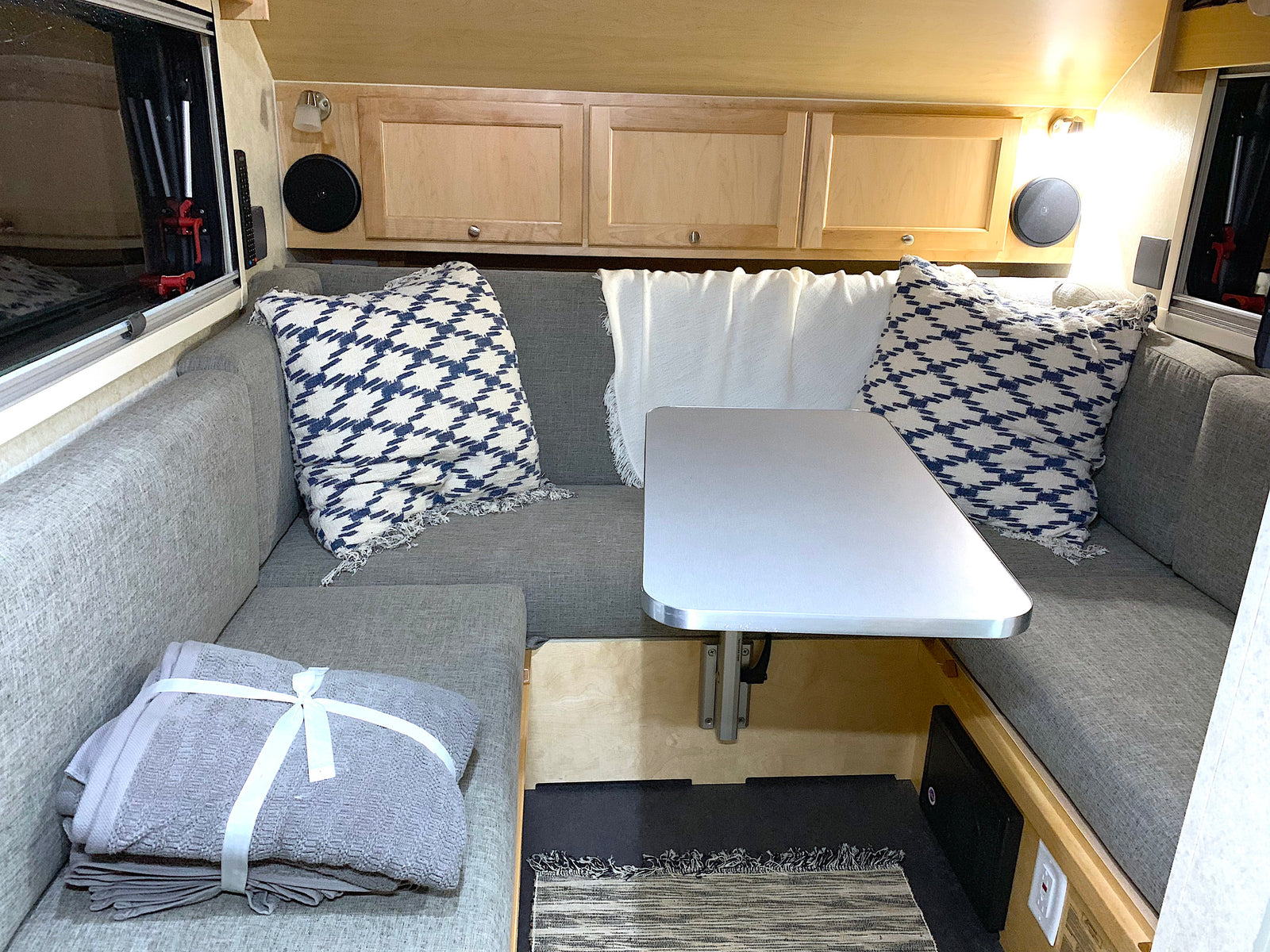 Step into this cozy RV rental's interior, featuring grey dinette seating, a central table, and overhead cabinets.